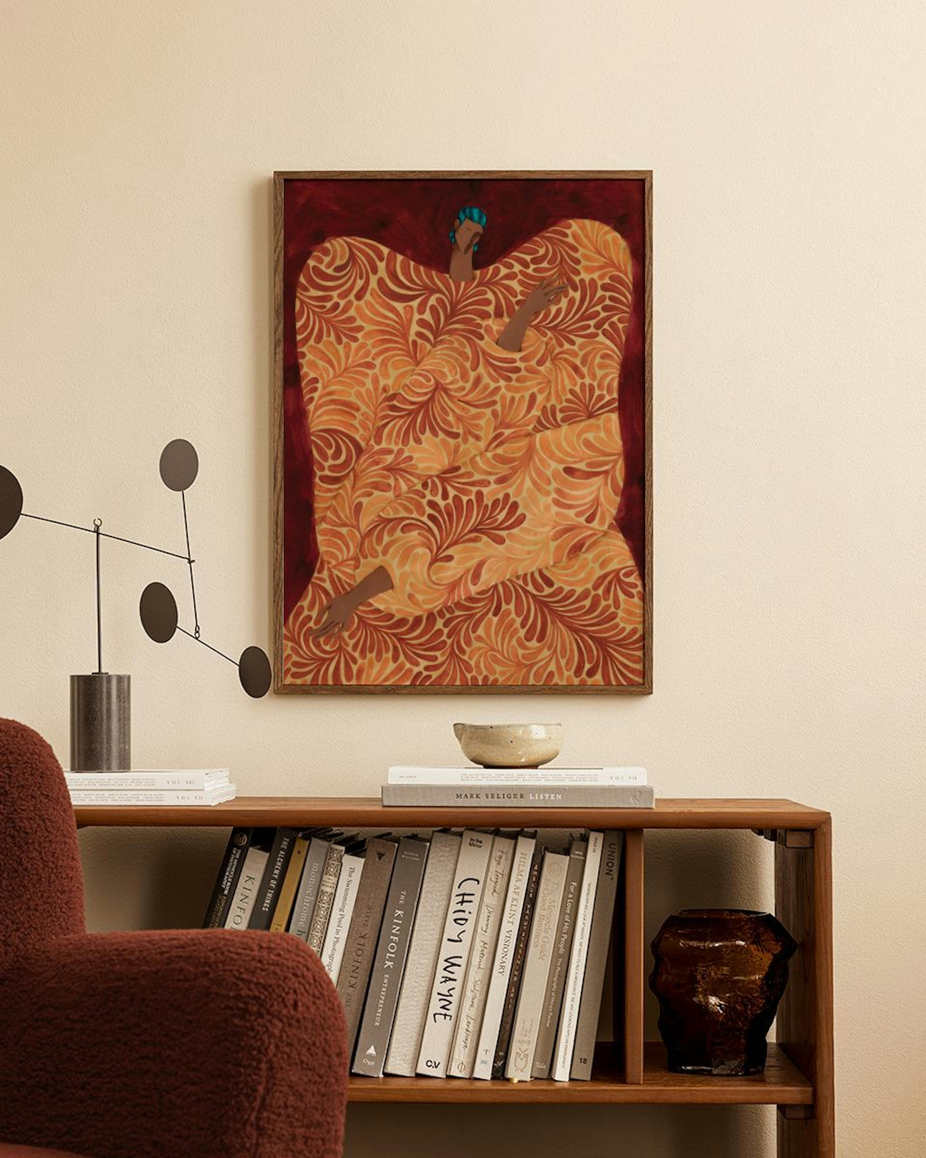 A print of a figure in a patterned orange and red robe against a dark red background, hanging above a wooden bookshelf.
