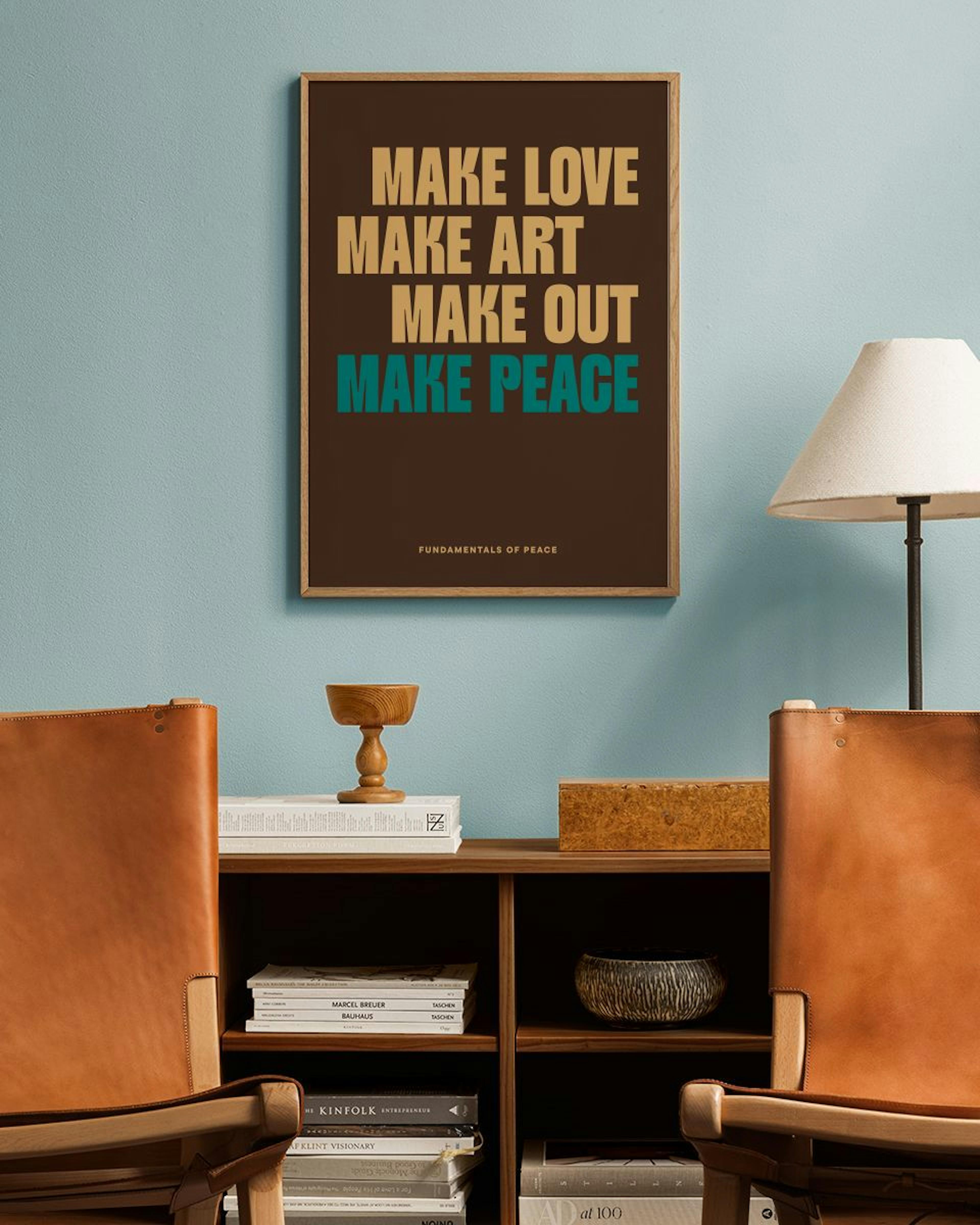 Póster marrón con texto beige y verde azulado MAKE LOVE MAKE ART MAKE OUT MAKE PEACE, colgado sobre un estante de madera con lib