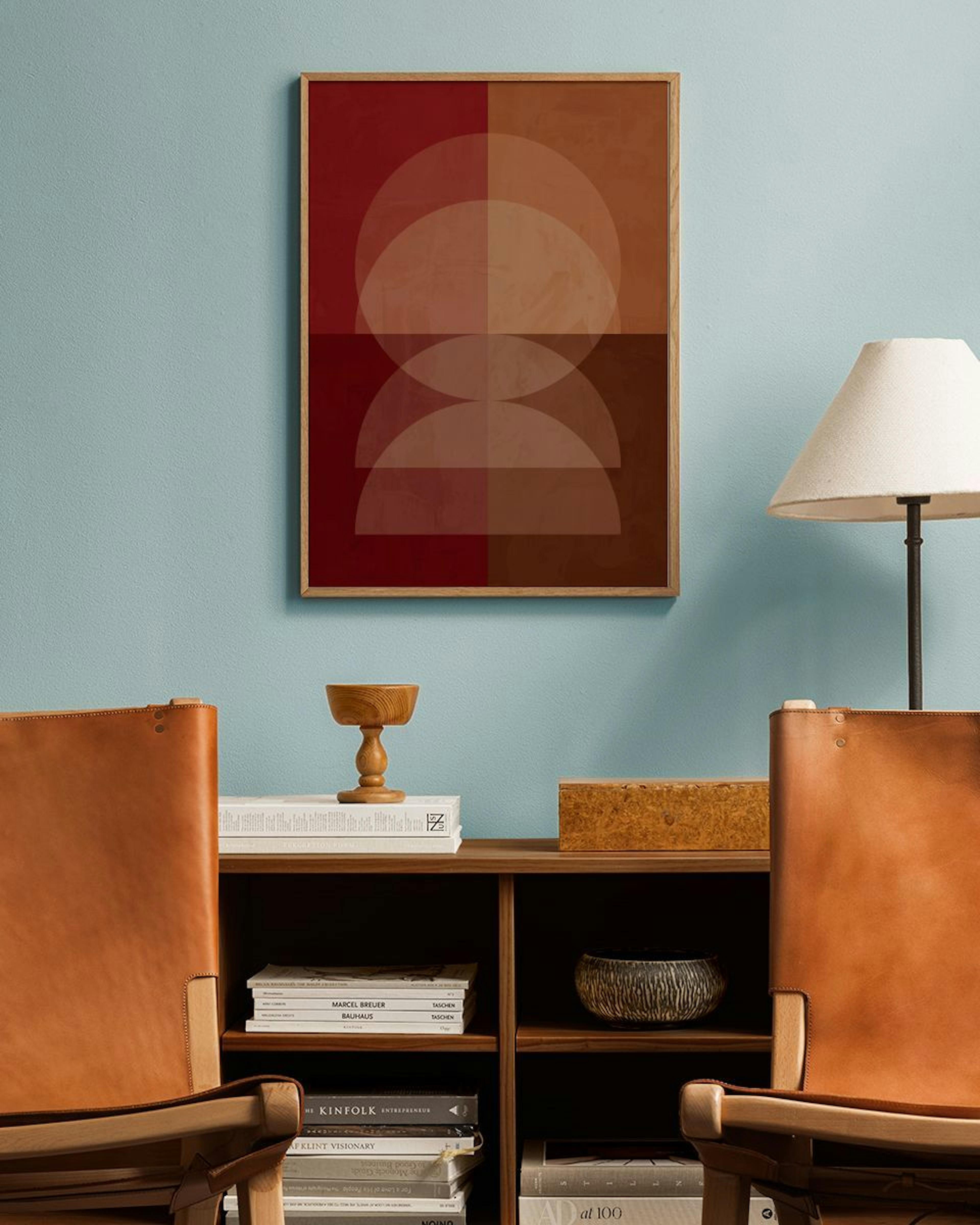 Póster de formas semicirculares superpuestas en tonos rojos y marrones, colgado en una pared azul claro sobre una estantería de 
