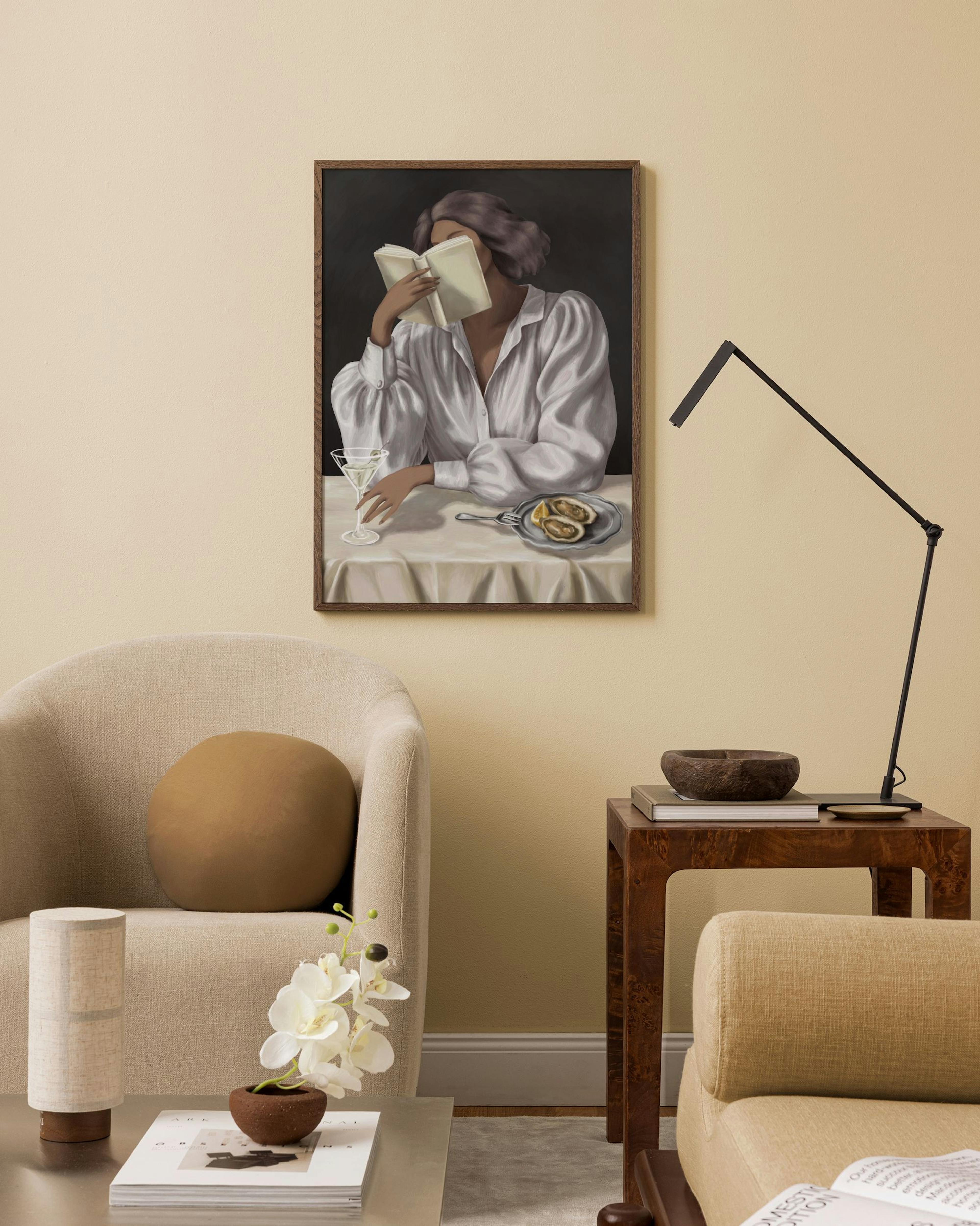 A print of a person in a white shirt reading a book with a martini and lemon on a plate, hanging in a minimalist living room.
