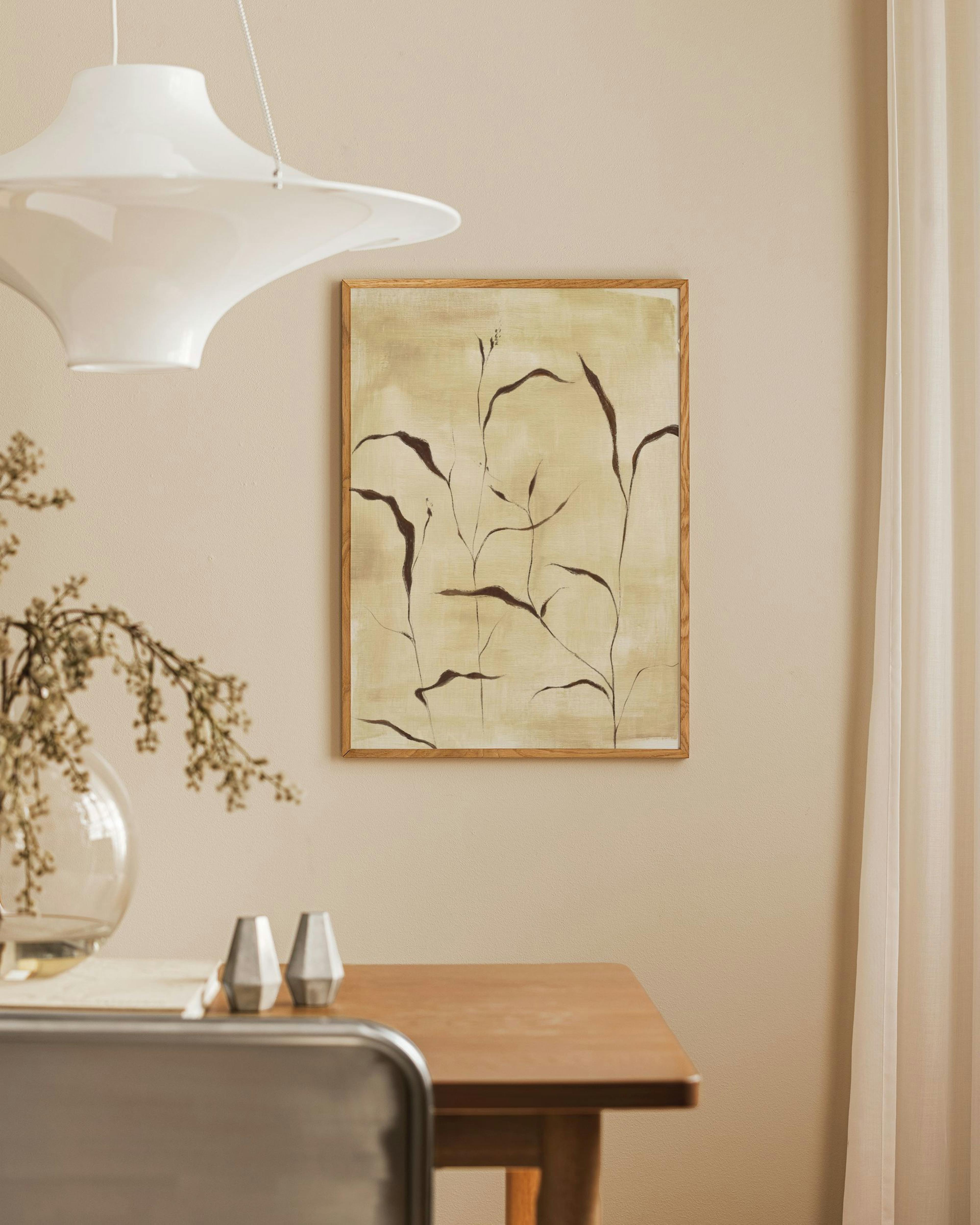 Botanical print with dark brown leaves on a textured light beige background, hanging in a dining room above a wooden table.