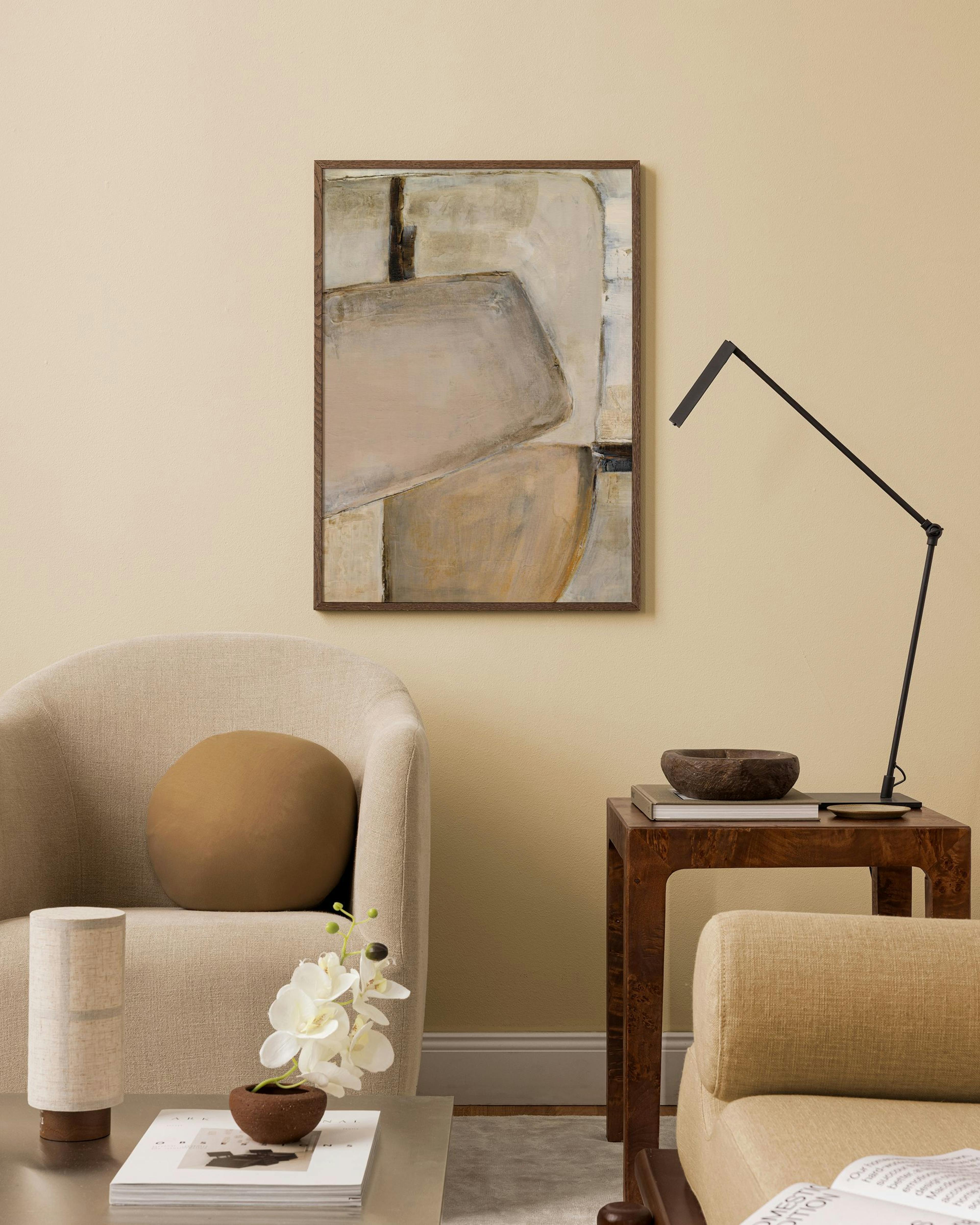 Póster de arte abstracto con formas geométricas en tonos neutros, colgando sobre un sillón en una sala moderna.