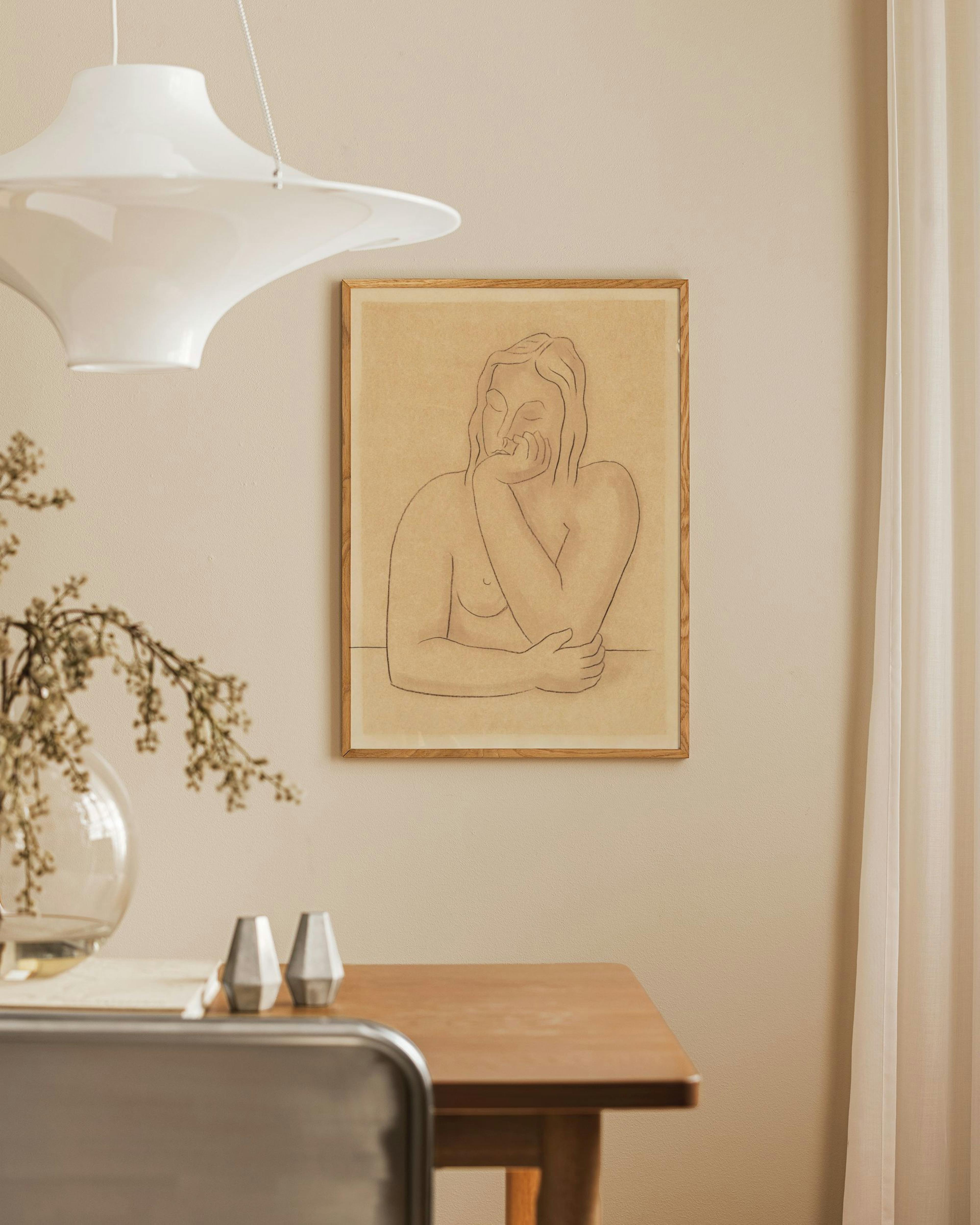 Póster de dibujo de figura femenina en contorno negro sobre fondo beige, colgando en una pared clara sobre una mesa de madera.
