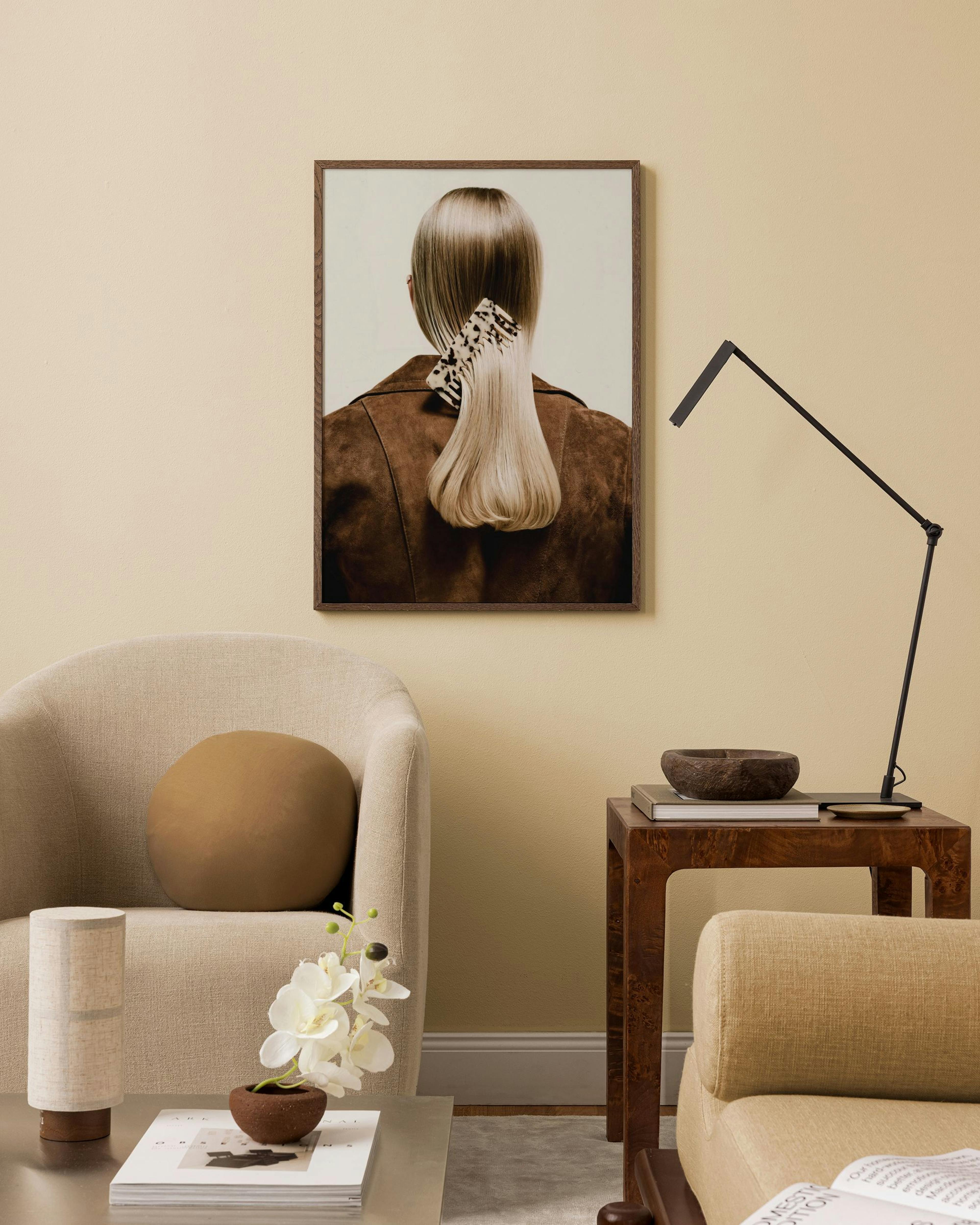 Póster de una mujer con cabello rubio y una chaqueta café, exhibido en una sala de estar moderna con muebles beige y una lámpara