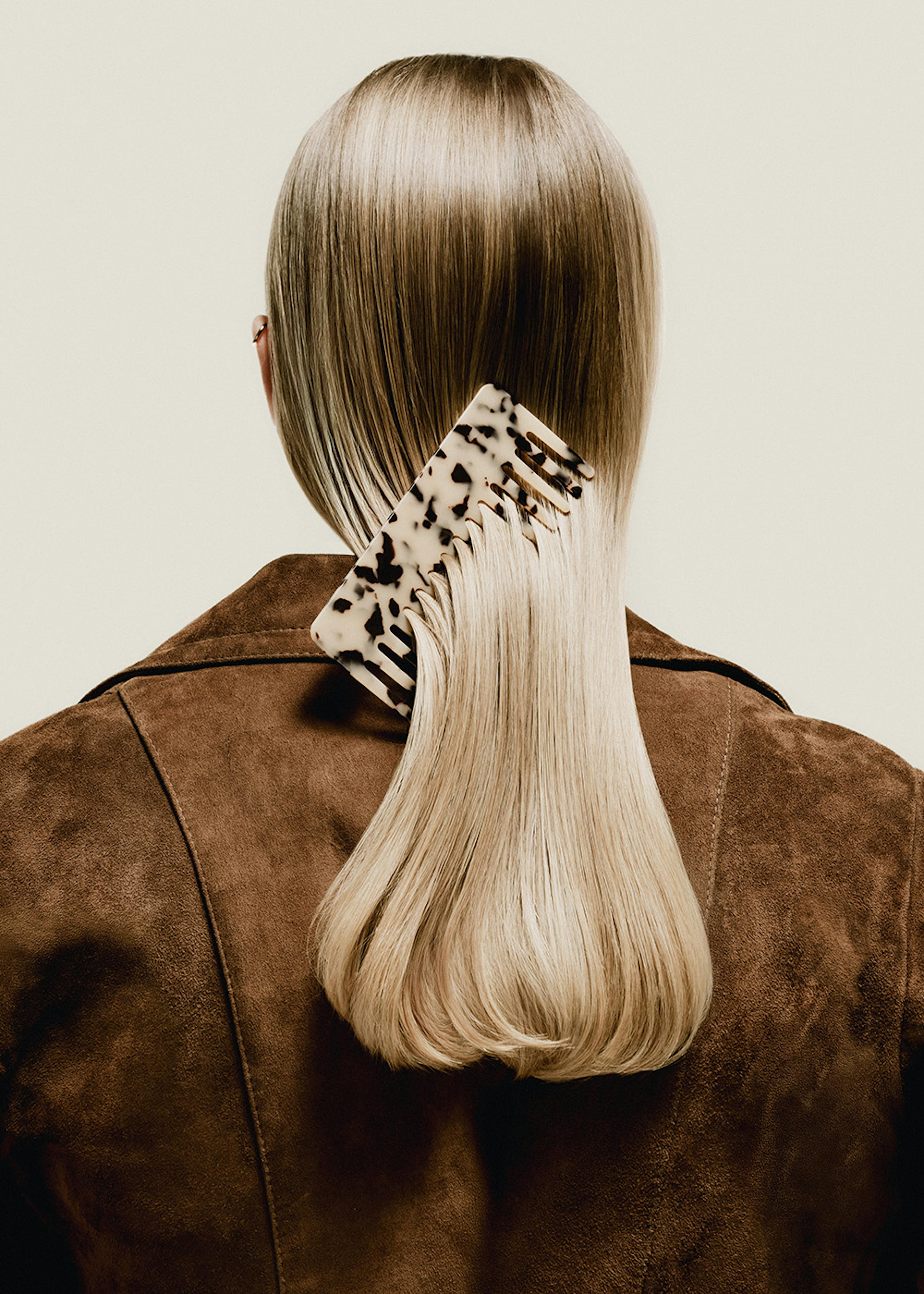 Un póster de la espalda de una mujer con cabello rubio liso y un peine de concha de tortuga en el cabello, vestida con una chaqu