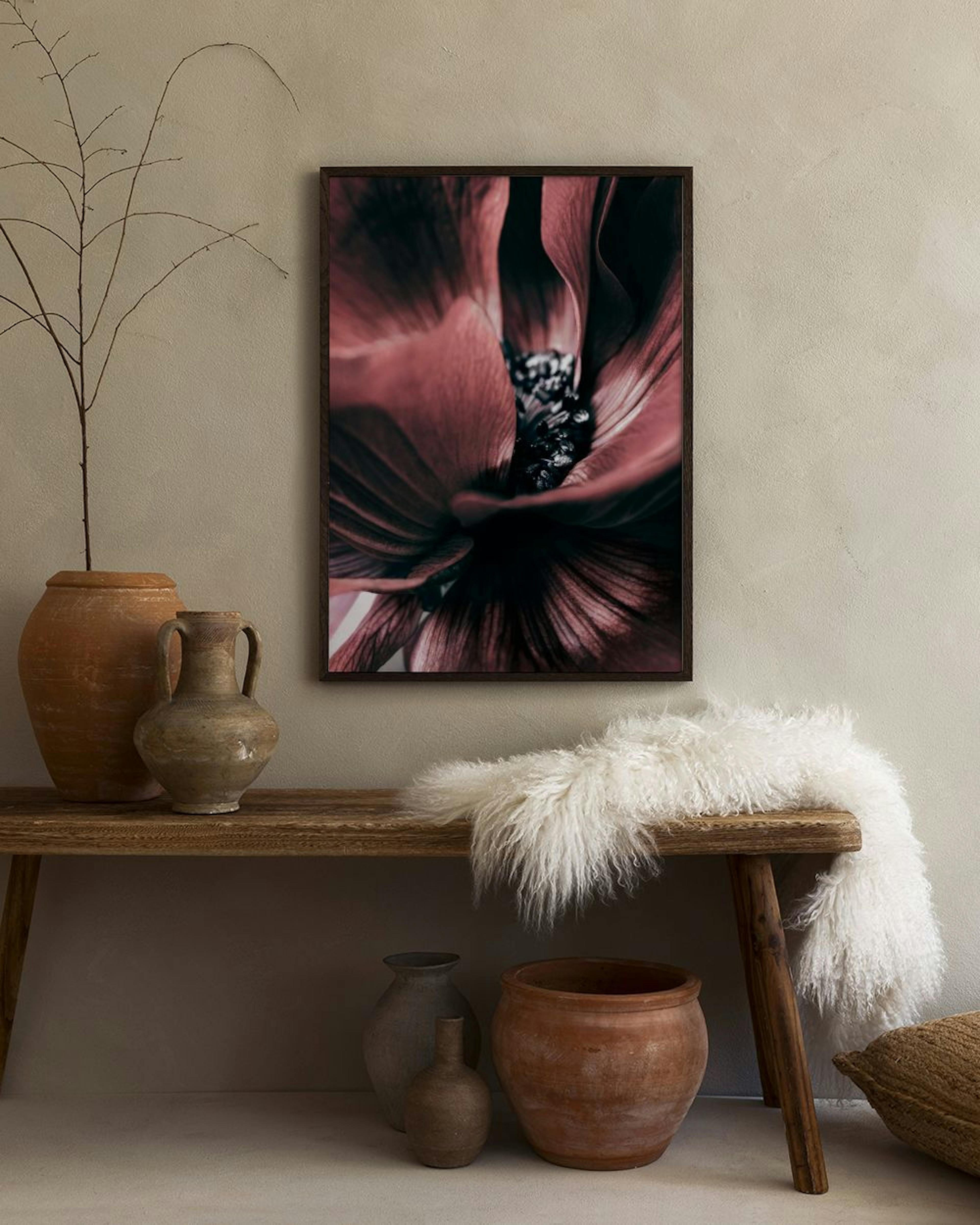 A print of a dark pink flower with black details, displayed on a light grey wall in a modern living space with a dark brown otto