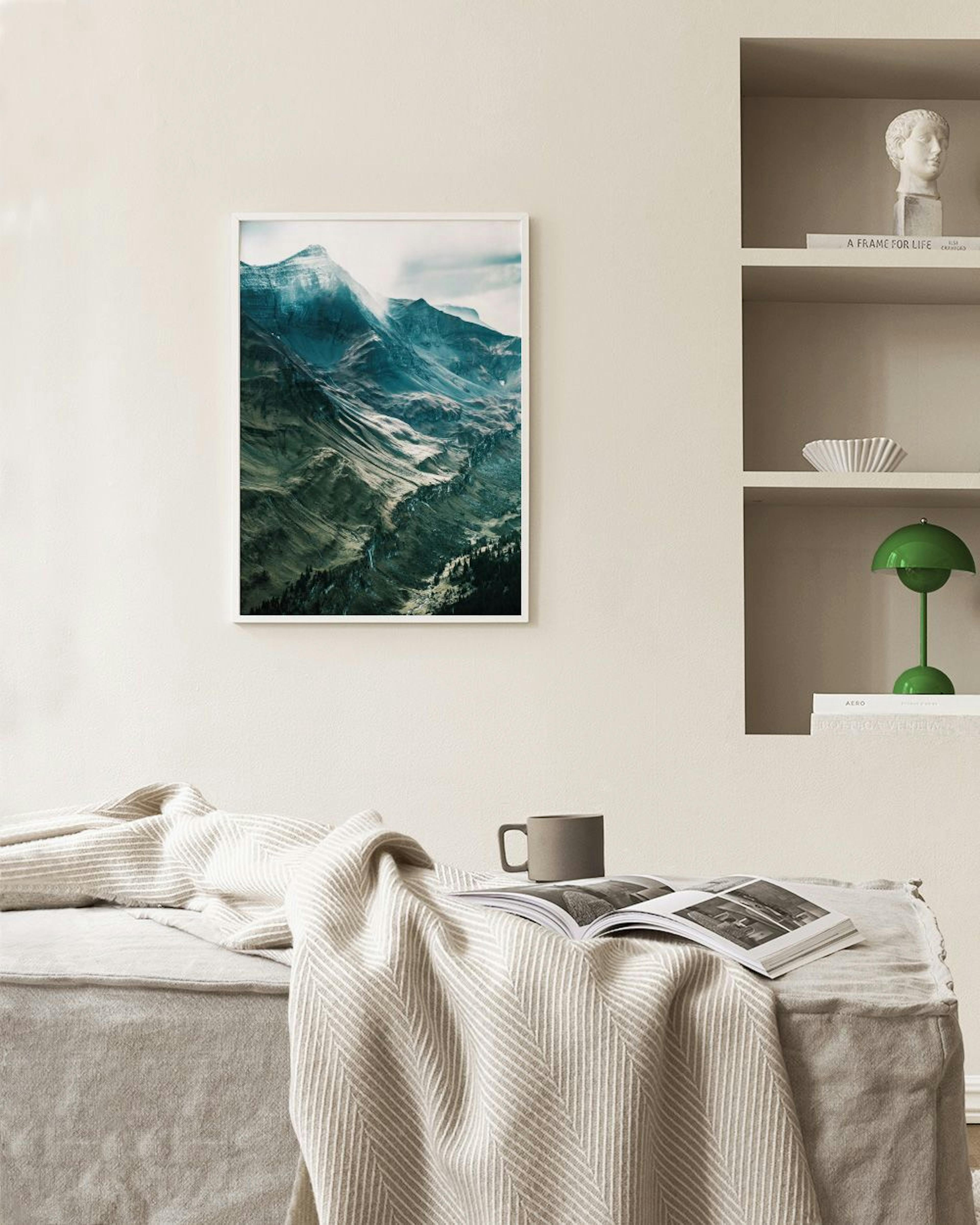 Poster con paesaggio montano innevato e valli verdi, appeso sopra una poltrona in velluto verde e un vaso.