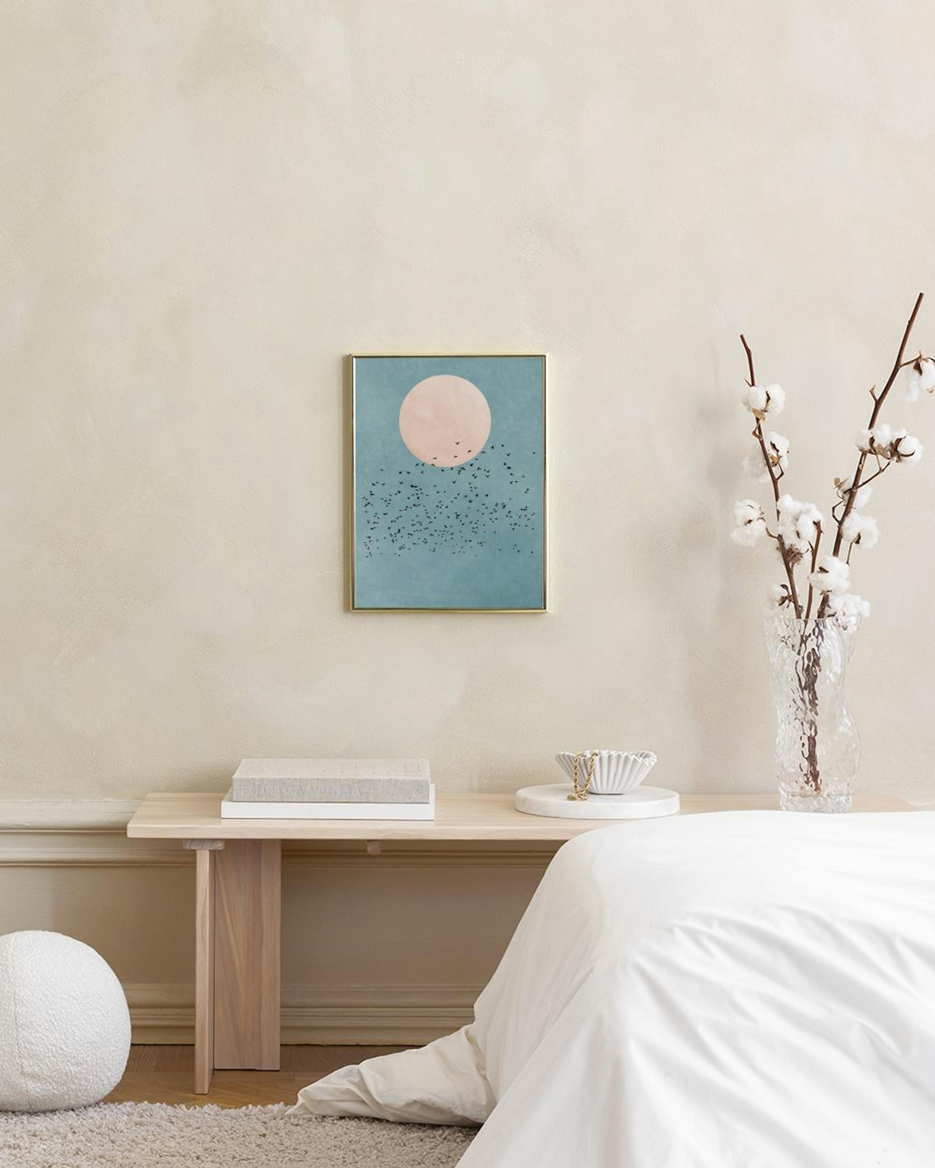 A print of a peach-colored full moon and a flock of birds against a textured blue sky, hanging above a small cork and black-legg