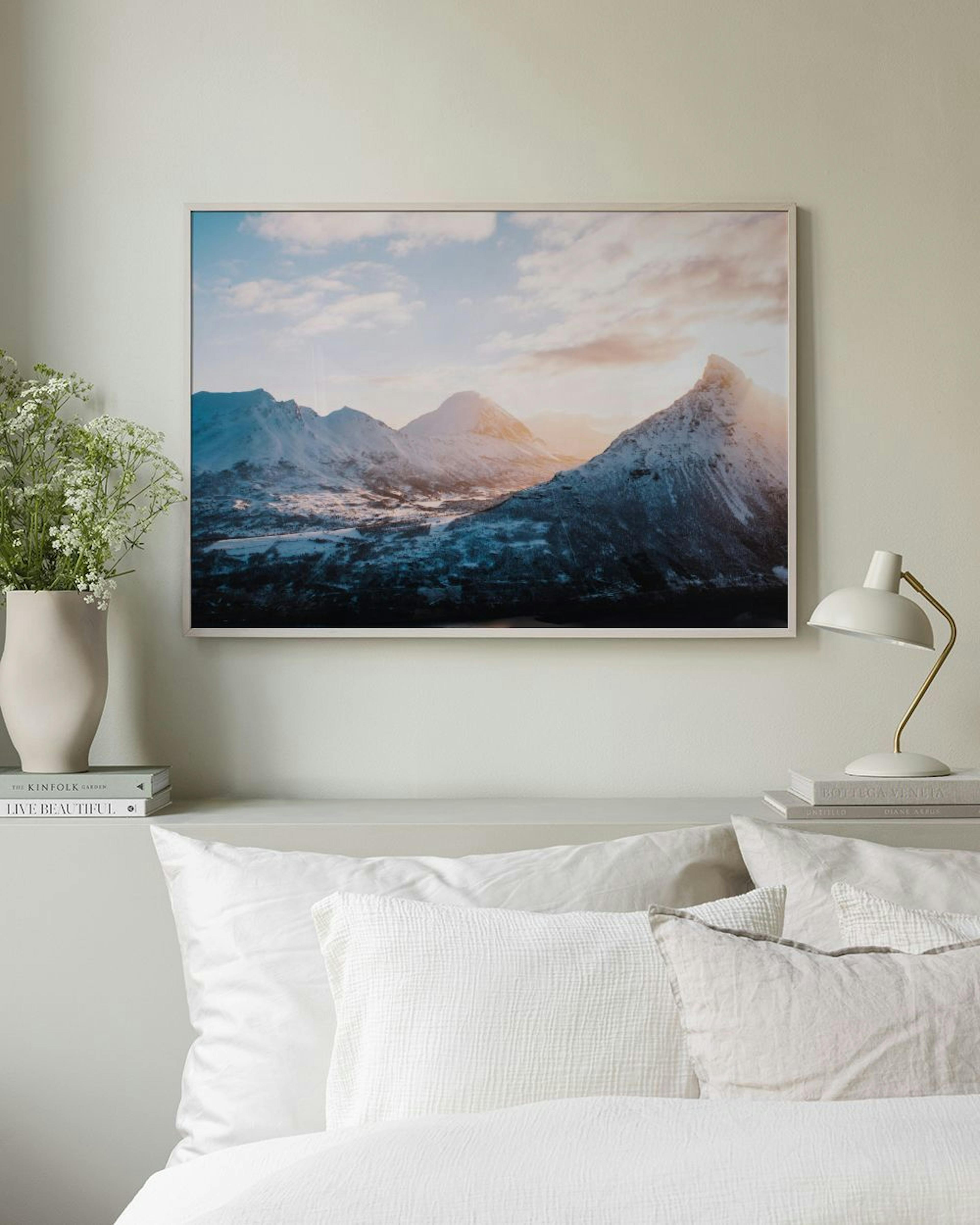 Póster de montañas nevadas con el sol brillando sobre el pico, colgado sobre un mueble blanco con jarrones.