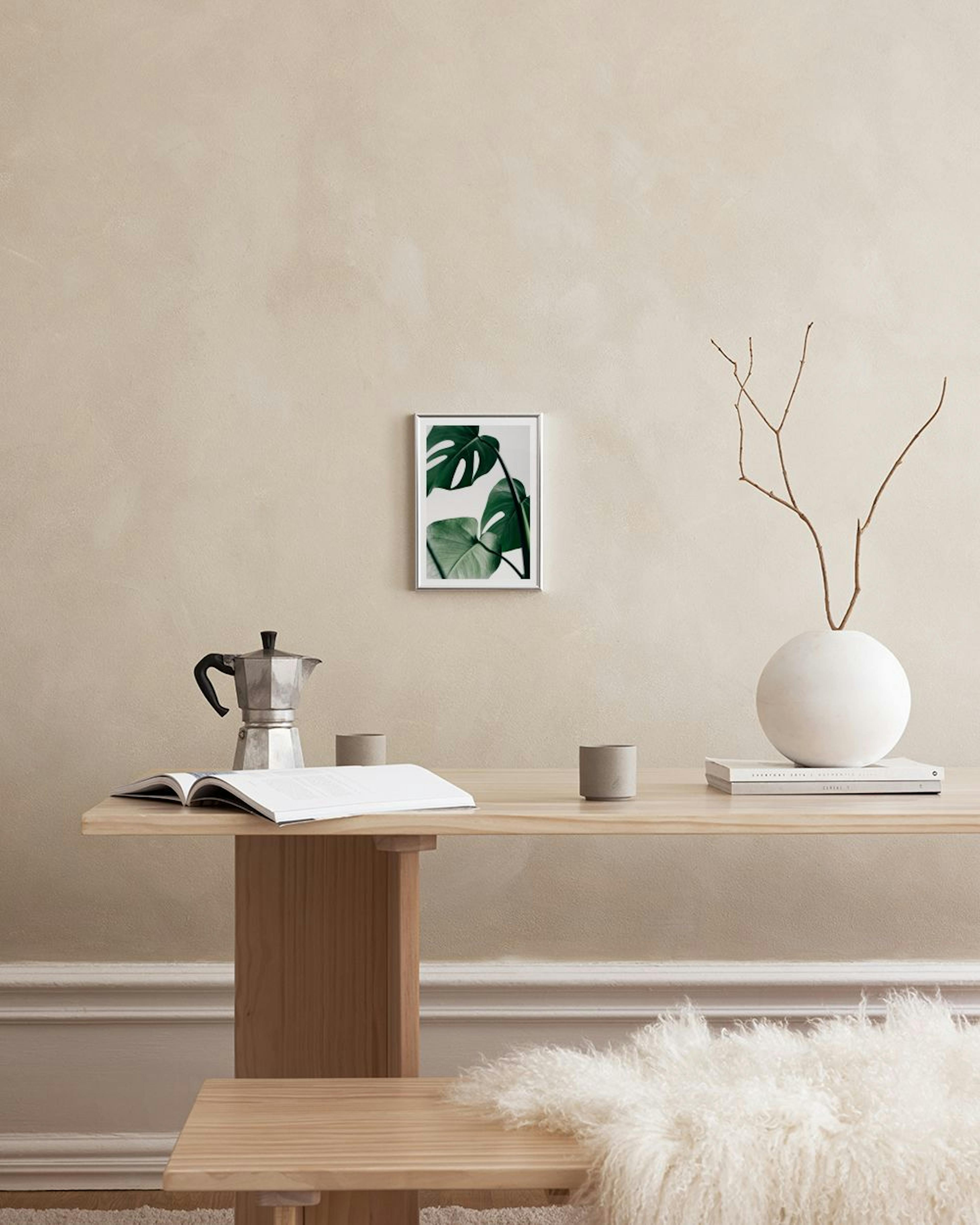 Affiche avec des feuilles de monstera vertes sur fond blanc, accrochée à une grille murale dans une pièce moderne.