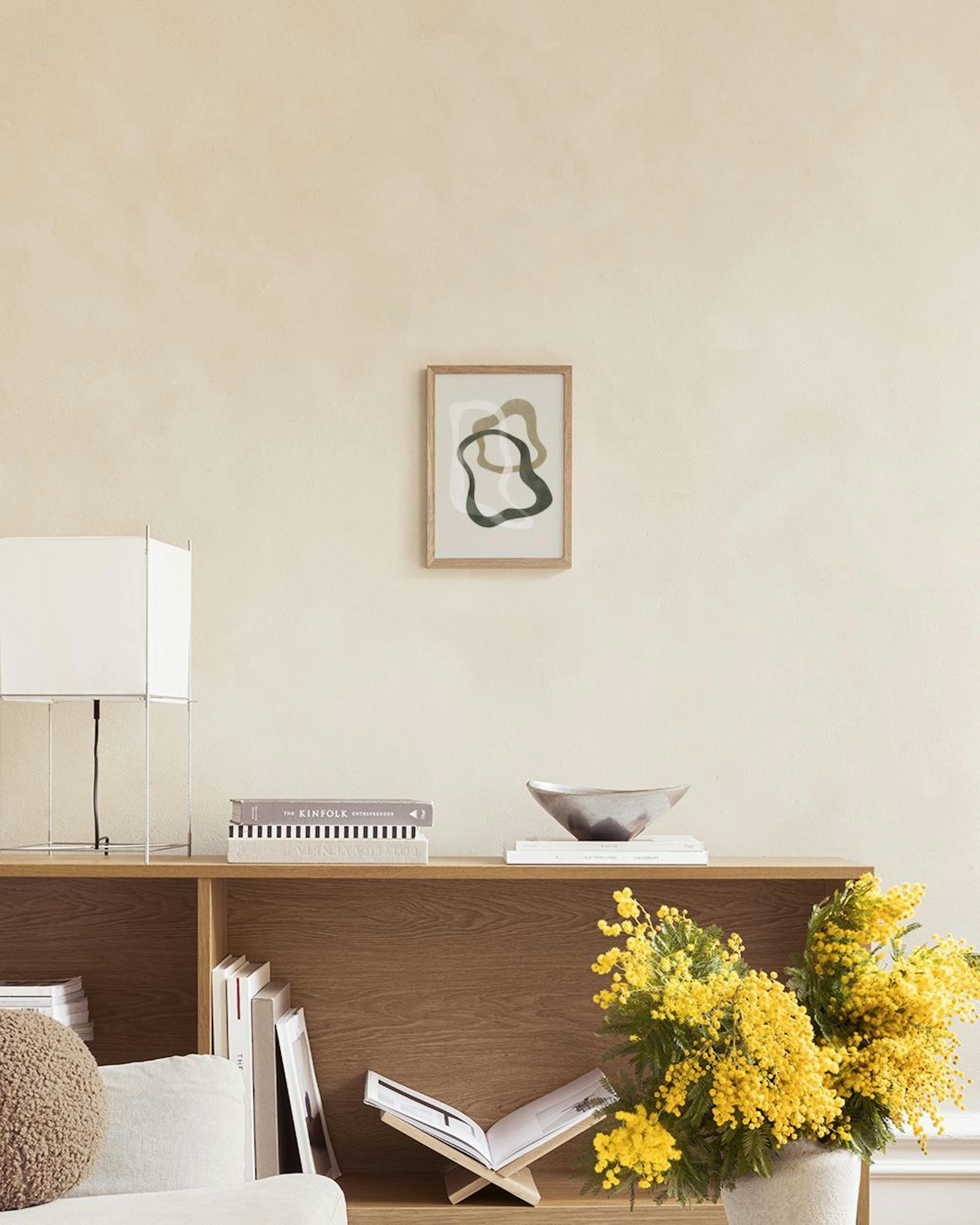 Affiche avec des formes organiques vertes et beiges, et des lignes blanches flottantes, exposée au-dessus dune table avec des va
