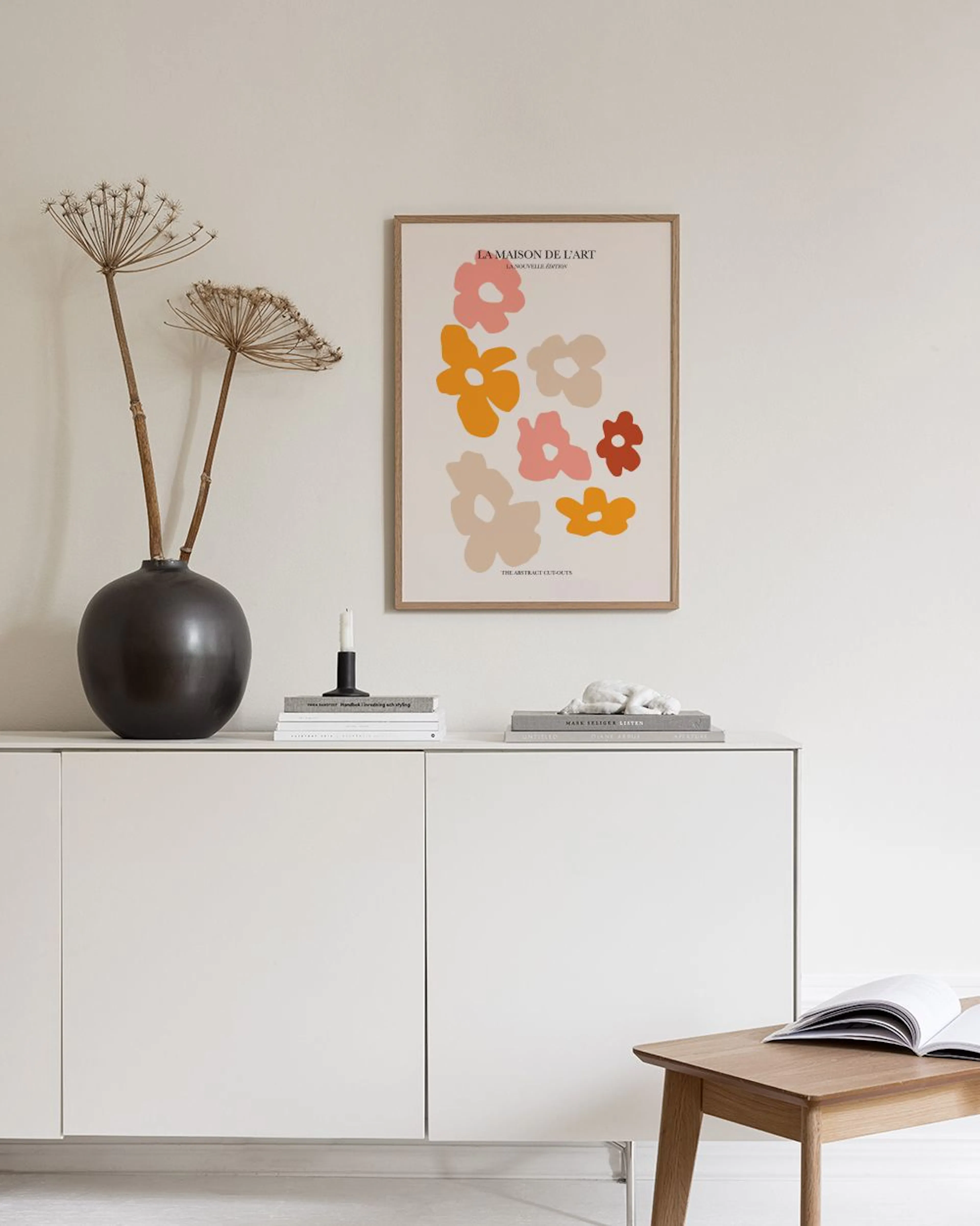 Poster mit abstrakten Blumen in Rosa, Orange und Beige, an einer grauen Wand über einem weißen Sideboard.
