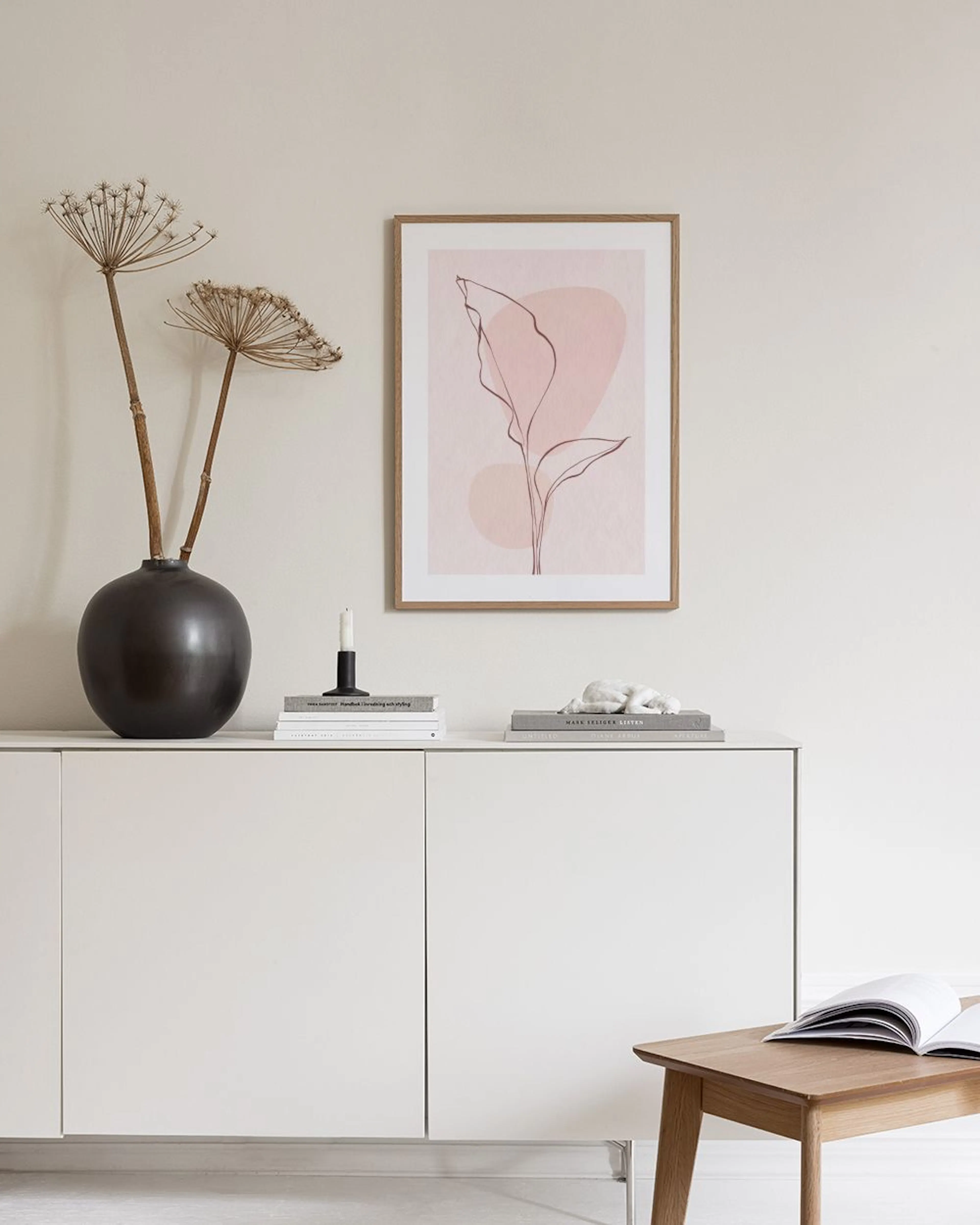Poster con linea singola di pianta su sfondo rosa tenue, esposto sopra un tavolino con vasi e libri.