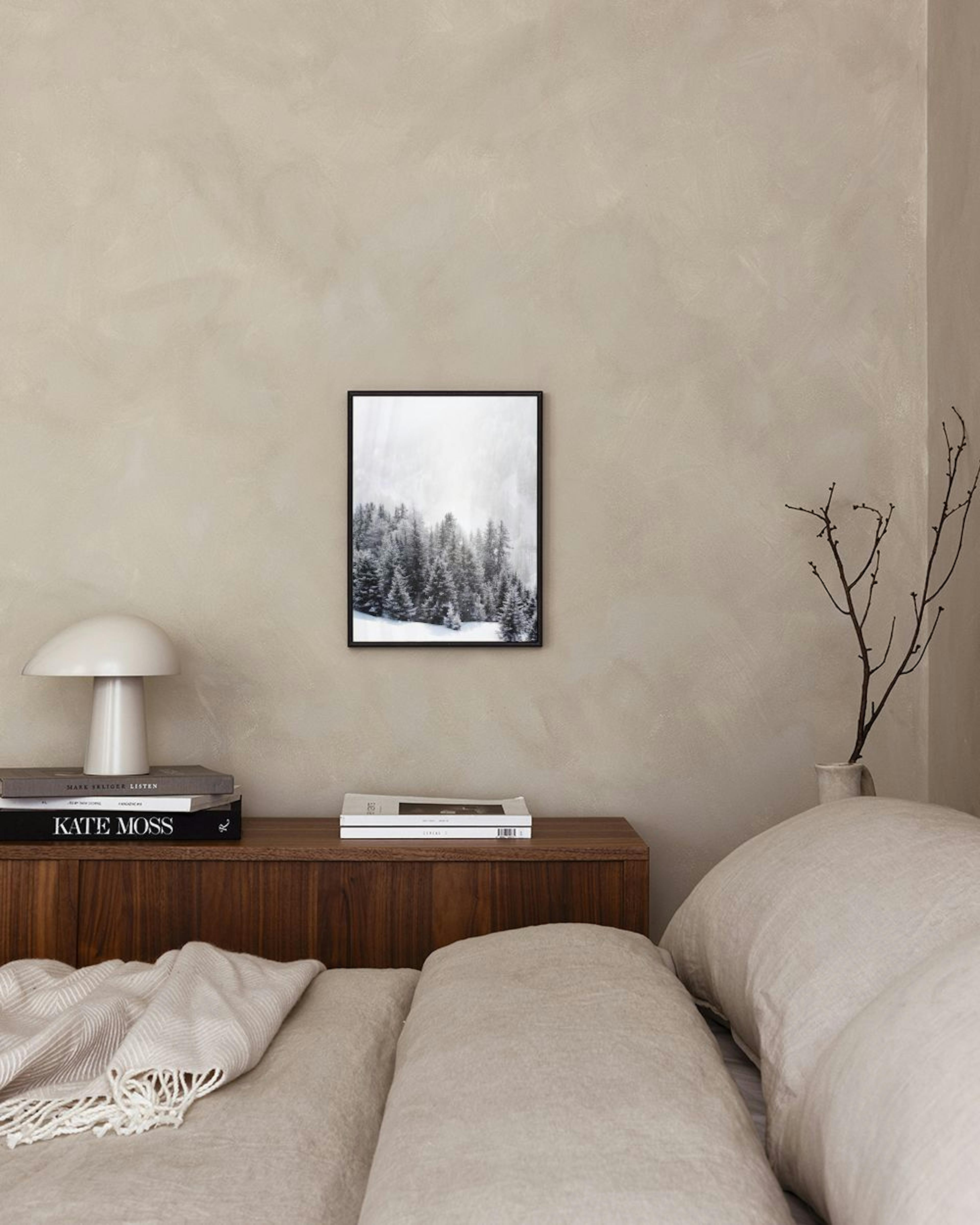 Poster con alberi innevati e foresta dinverno, appeso in una camera da letto sopra un letto con un libro.