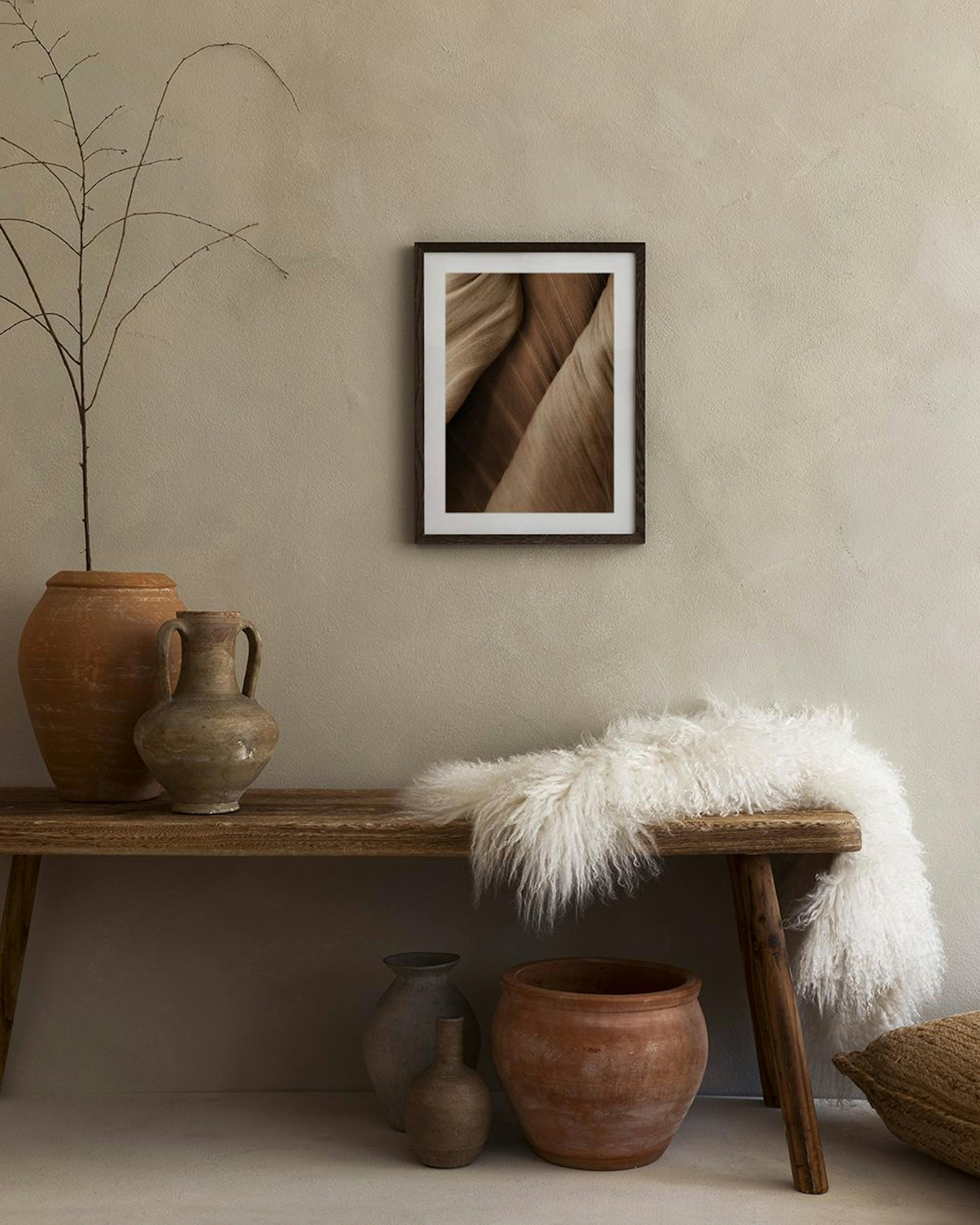 A print of brown palm tree leaves with natural textures, displayed above a light beige cabinet with decorative vases and books.