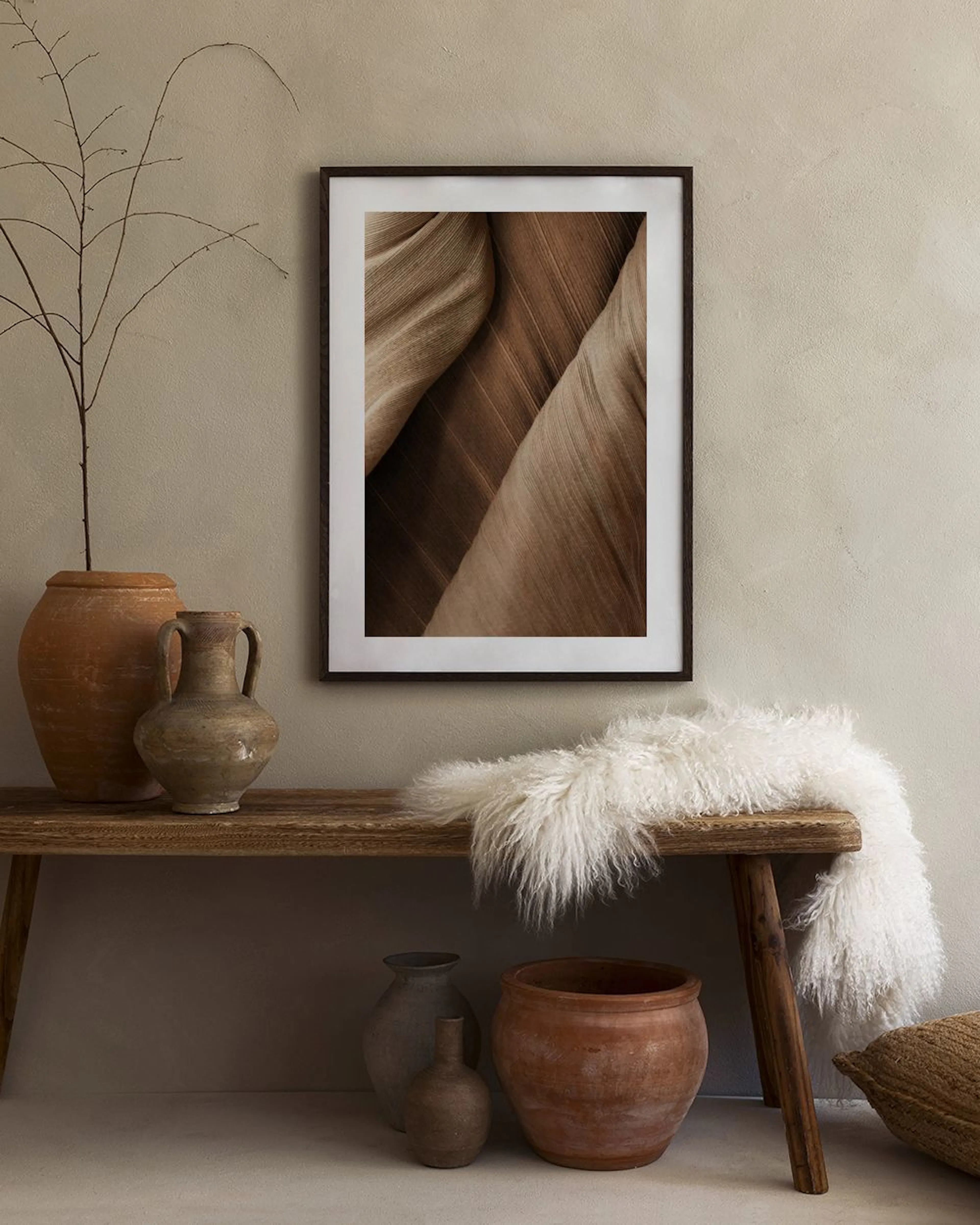 Un poster con texture di foglie marroni, appeso sopra una credenza beige con vasi e libri.