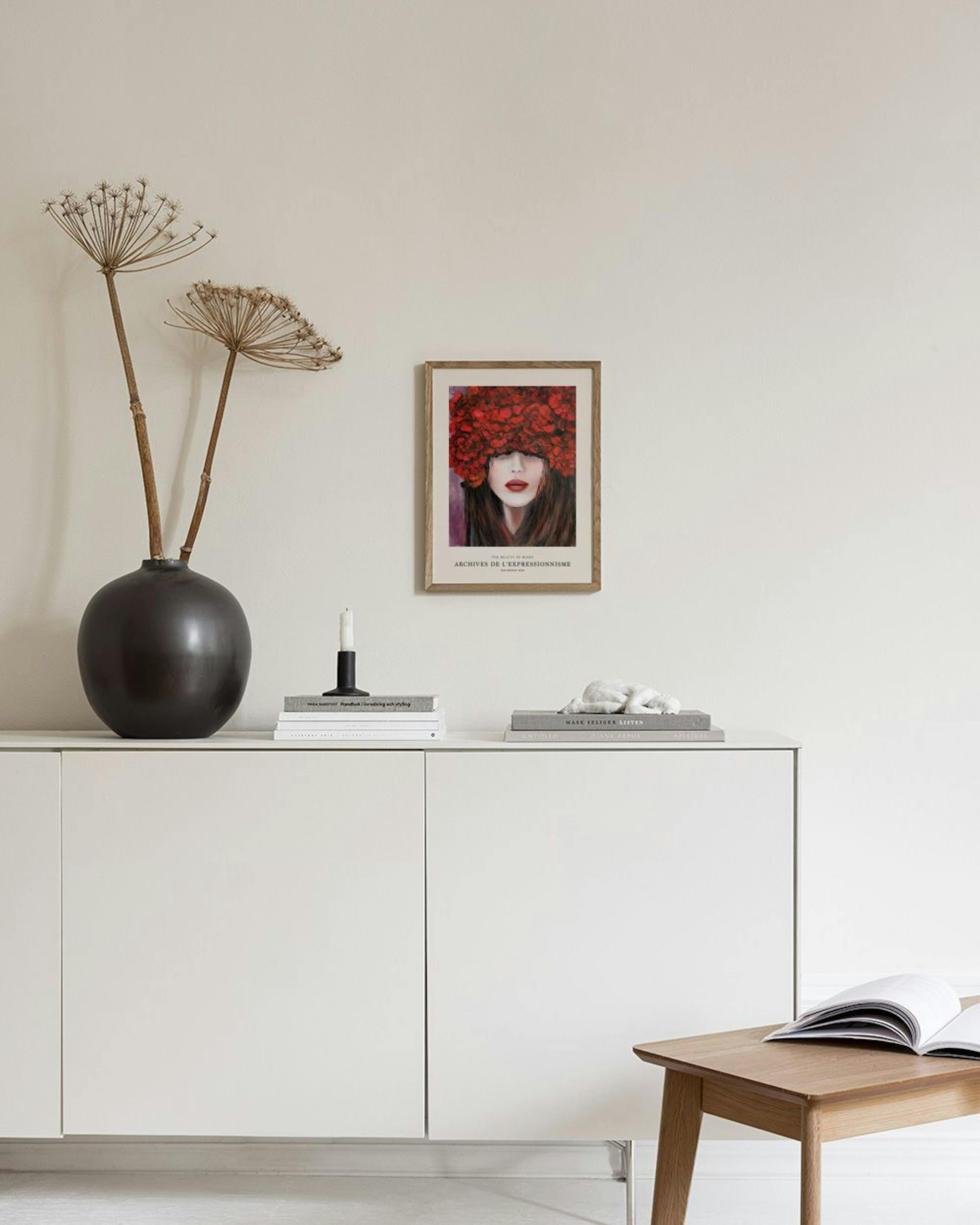 A print of a woman with red lips and a vibrant red floral headpiece, hanging above a white cabinet with decorative vases and boo