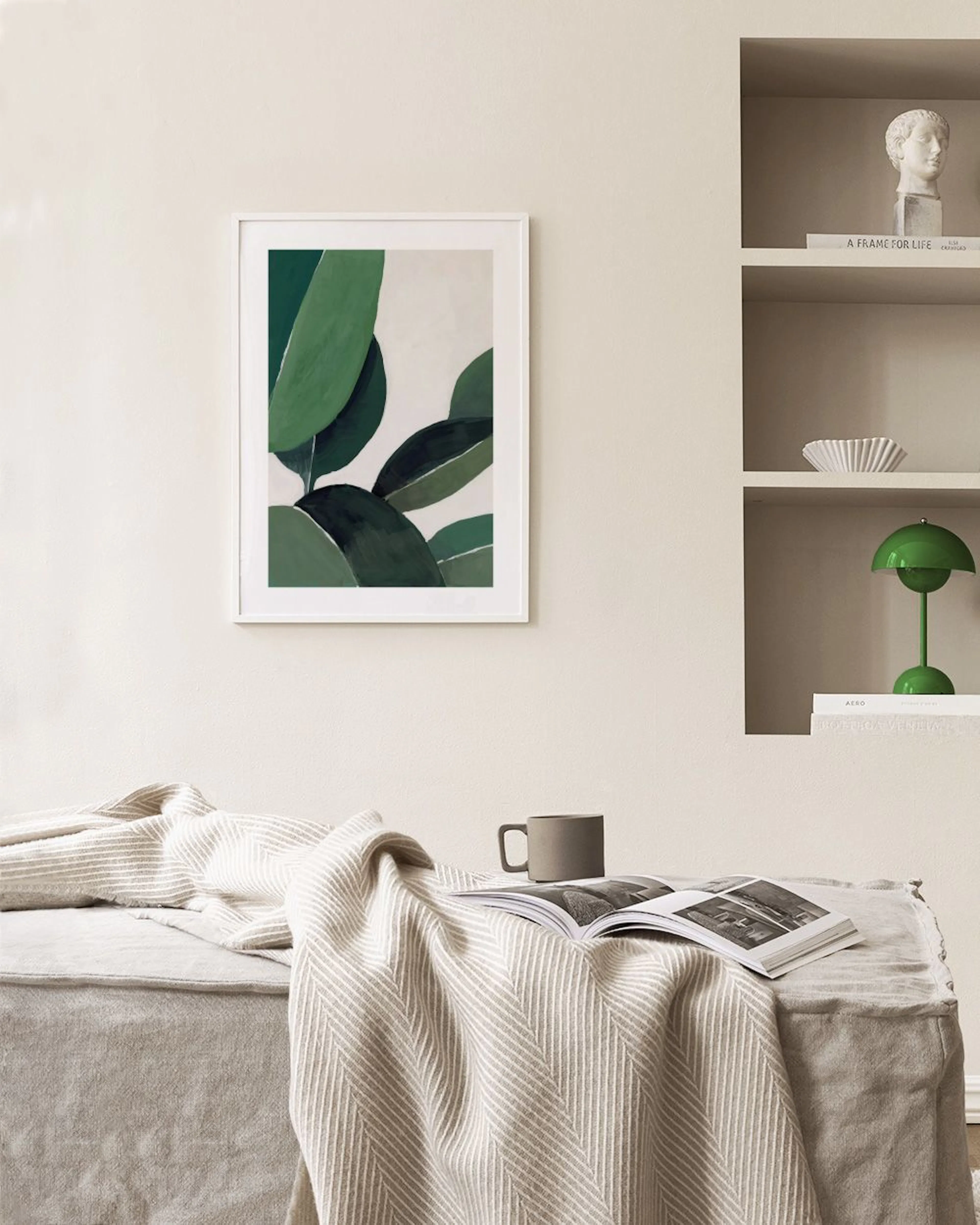Poster med gröna bladmotiv, hängande över en grön skänk med böcker och dekorationer.