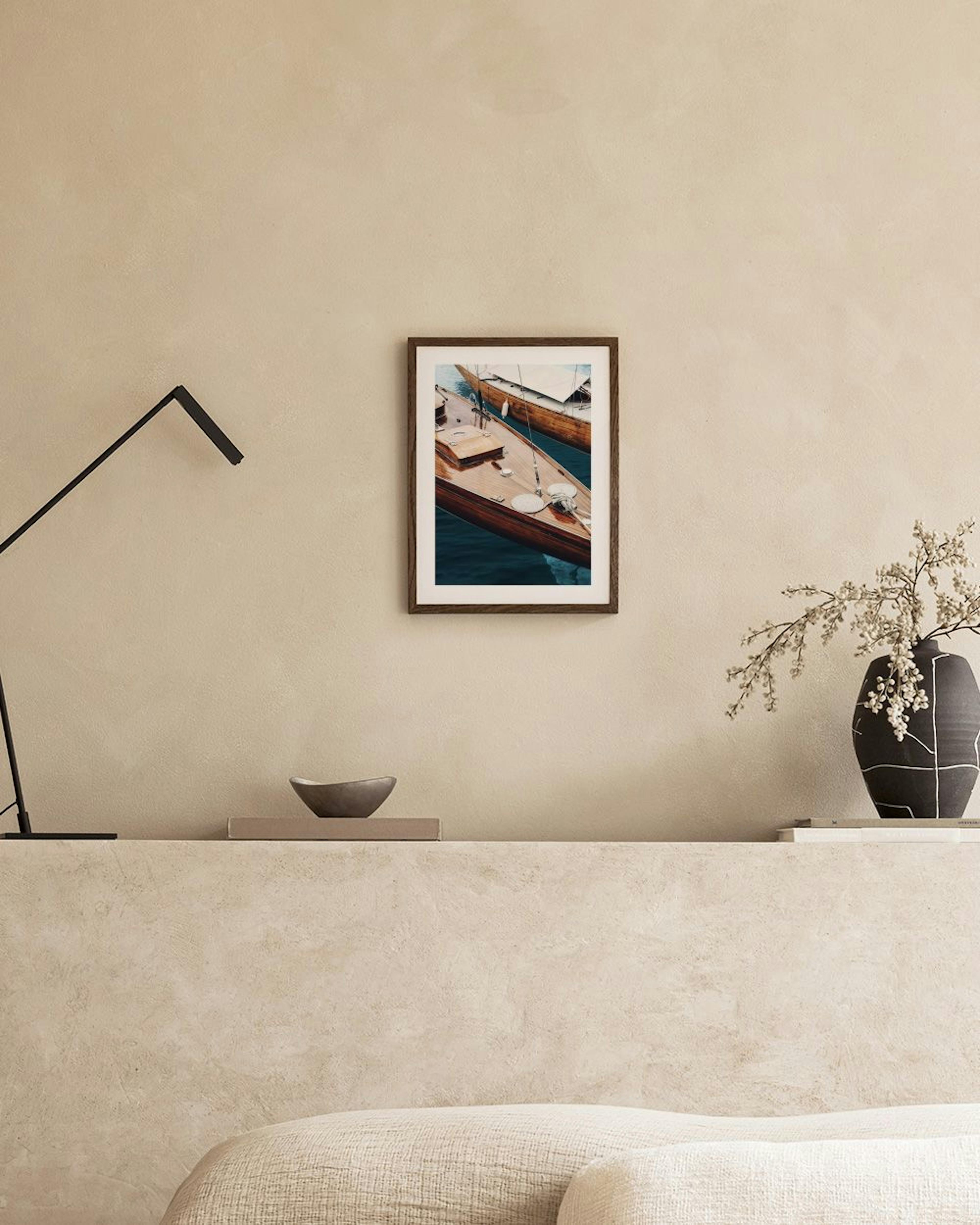 A print of two wooden boats on dark blue water, hanging above a bedside table in a bedroom.
