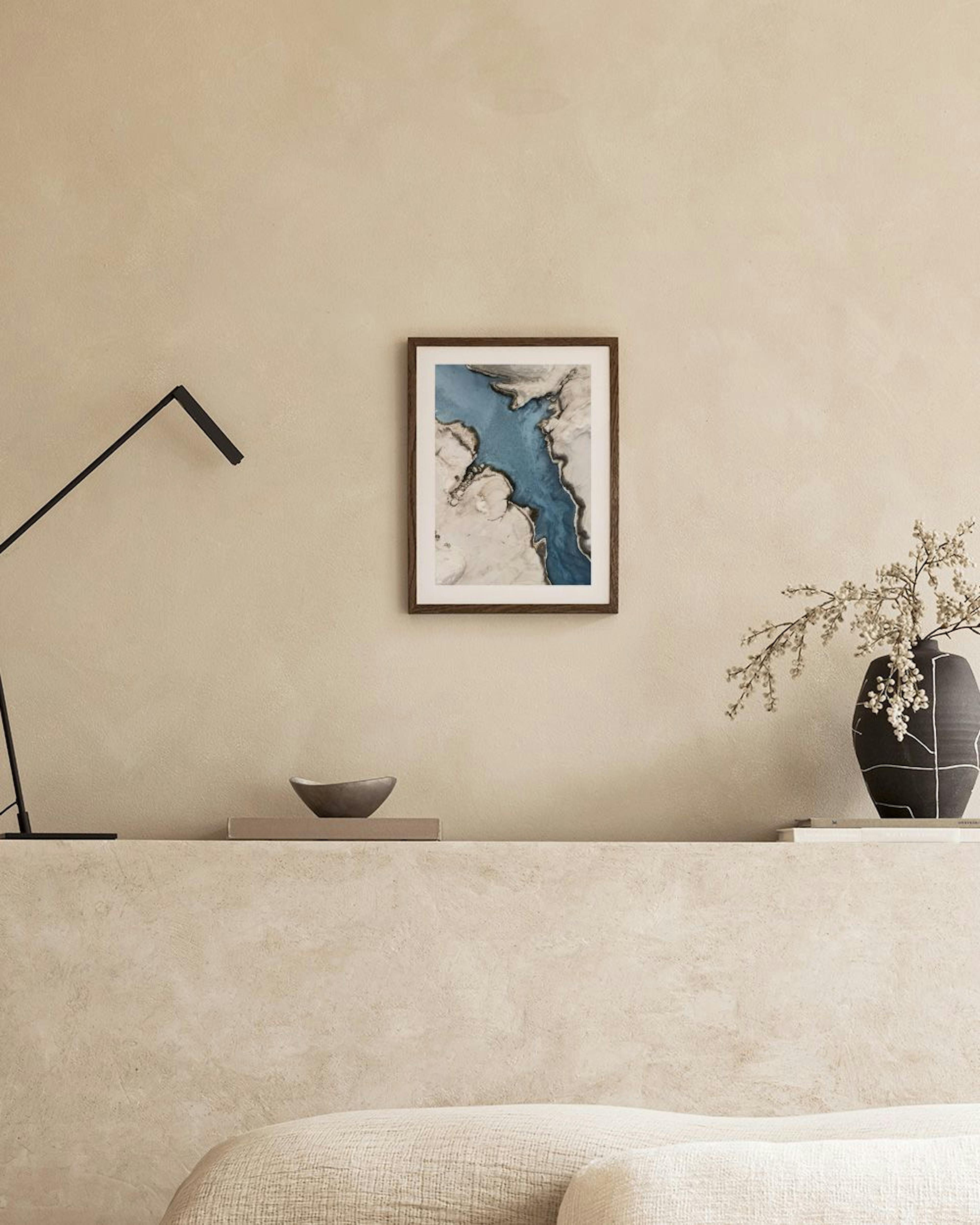 Poster mit abstraktem, blauem Flusslauf durch helle, beigefarbene Erdformationen, über einer Holzbank im Wohnzimmer.