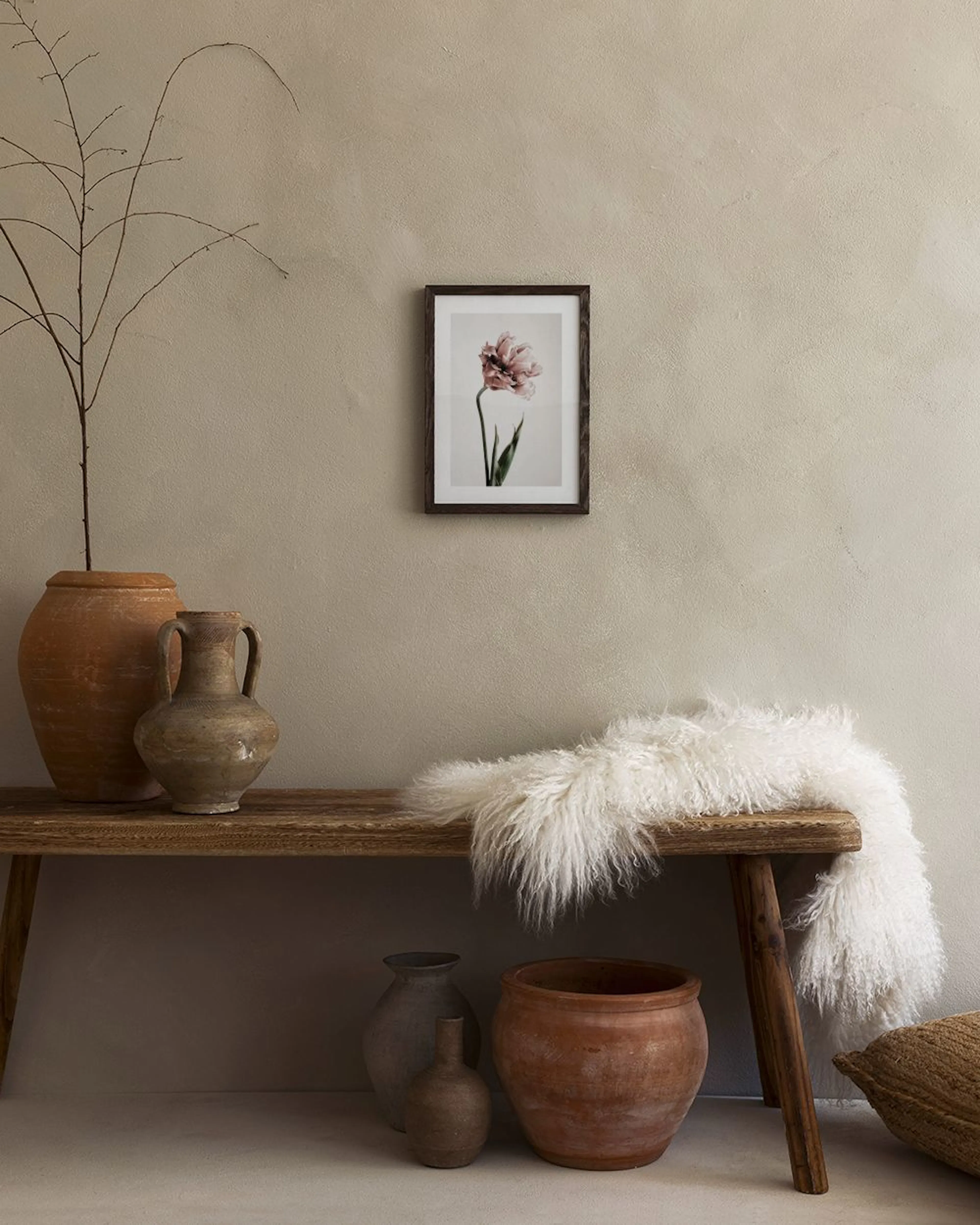 Poster van een zachtroze tulp met groene stengel en bladeren, hangend boven een blauw dressoir met vazen.