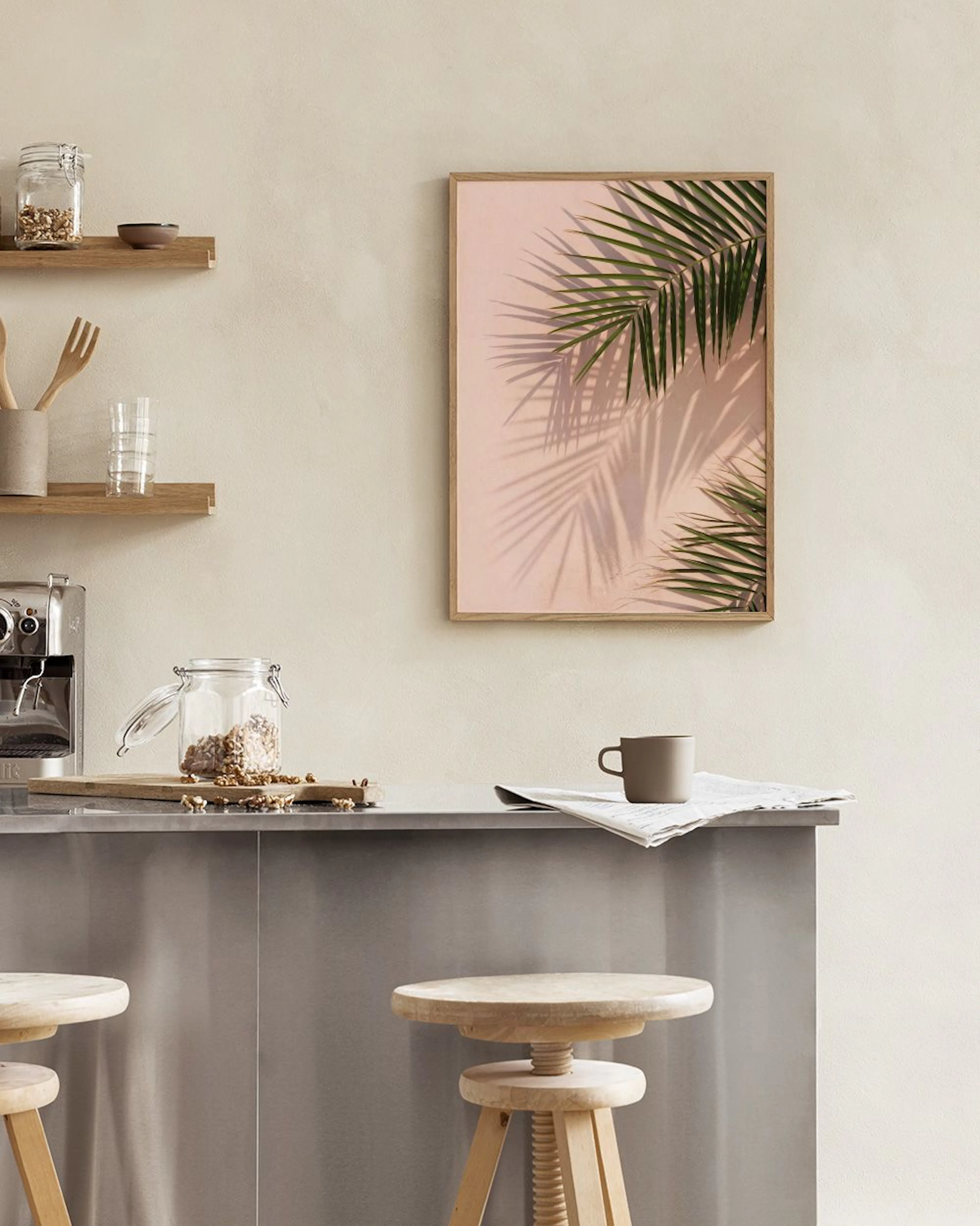A print of green palm fronds with shadows on a pink background, hanging above a teal velvet stool and black table with a white v