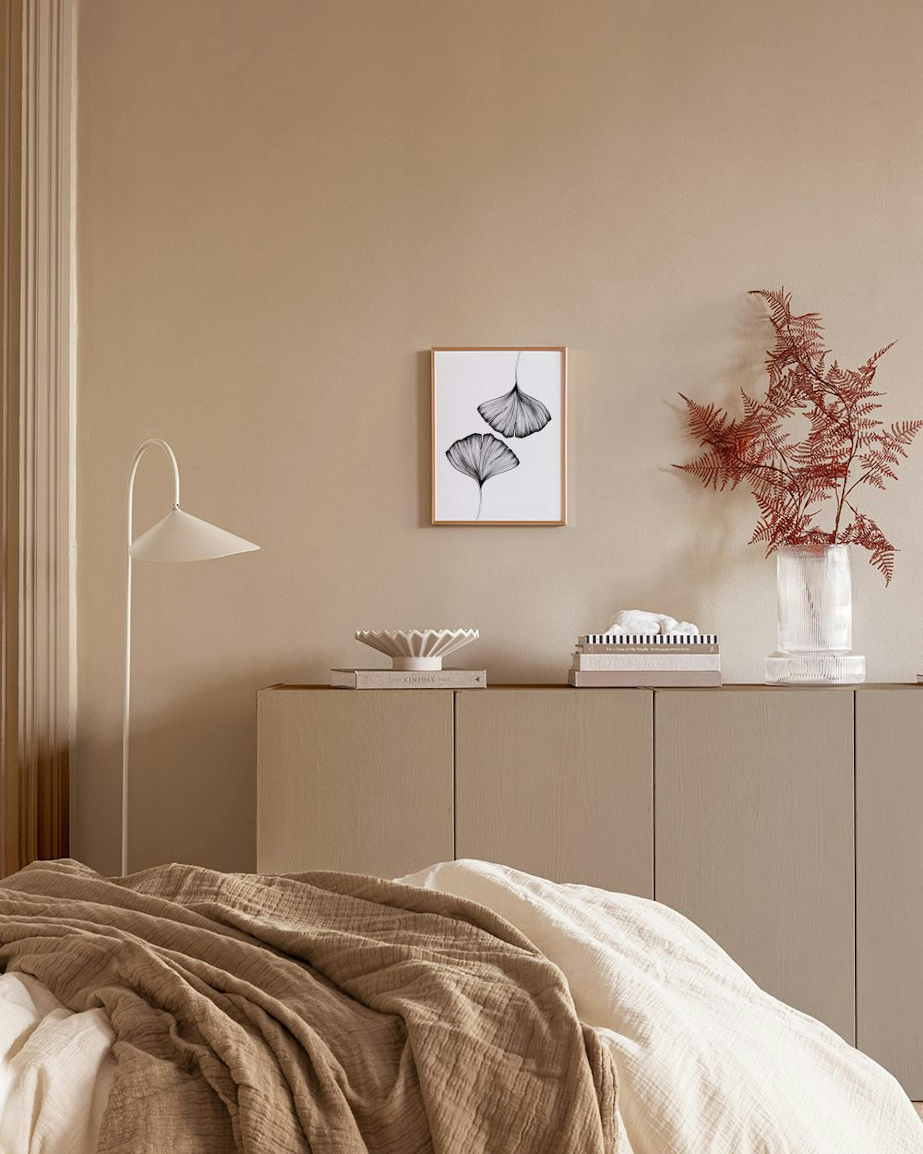 Plakat med to detaljerede, sorte Ginkgo-blade, der hænger på en mørkeblå væg med geometriske guldmønstre over en gylden rullebak