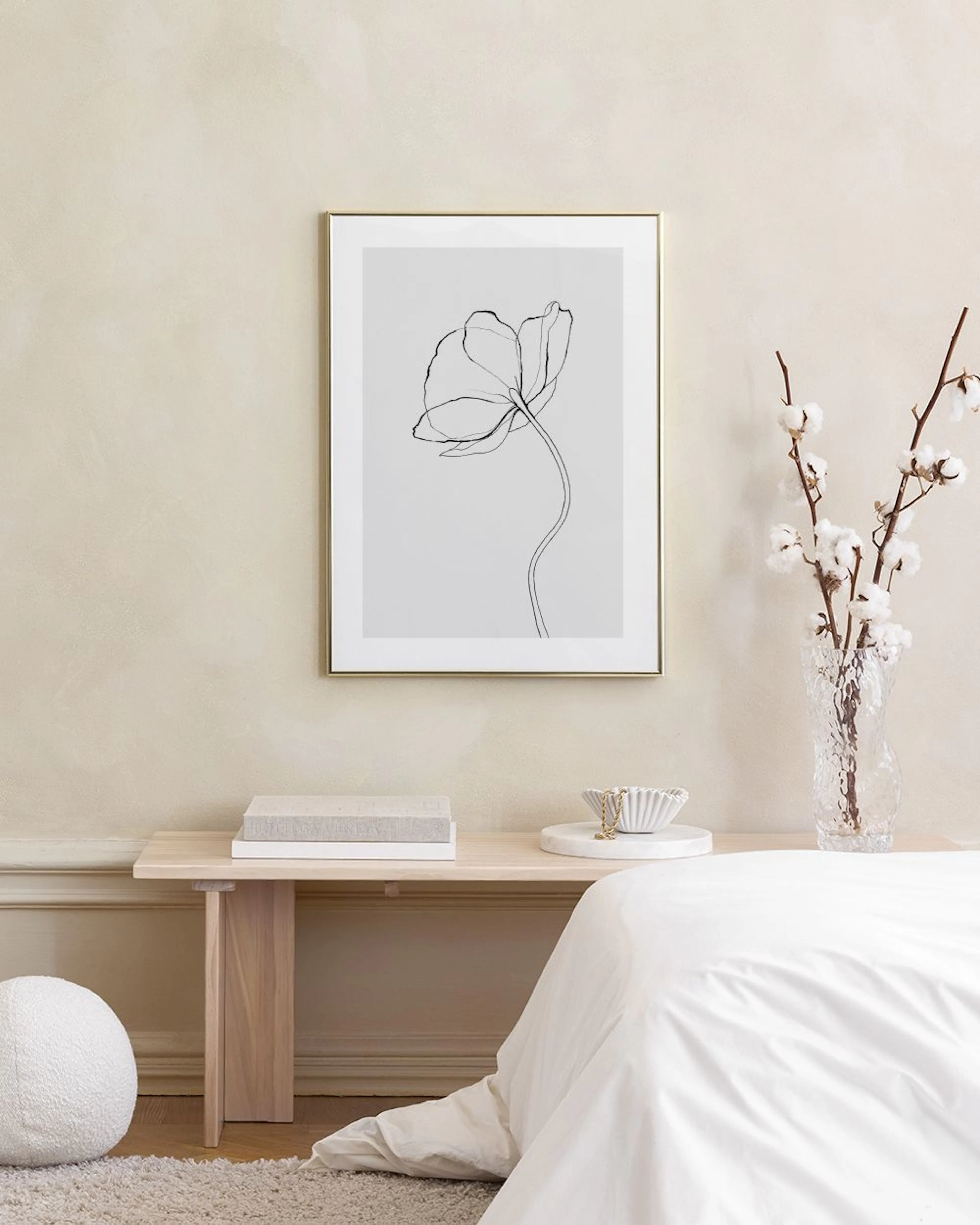 A minimalist flower line art print on a grey wall above a white cabinet, with a sofa and plants.