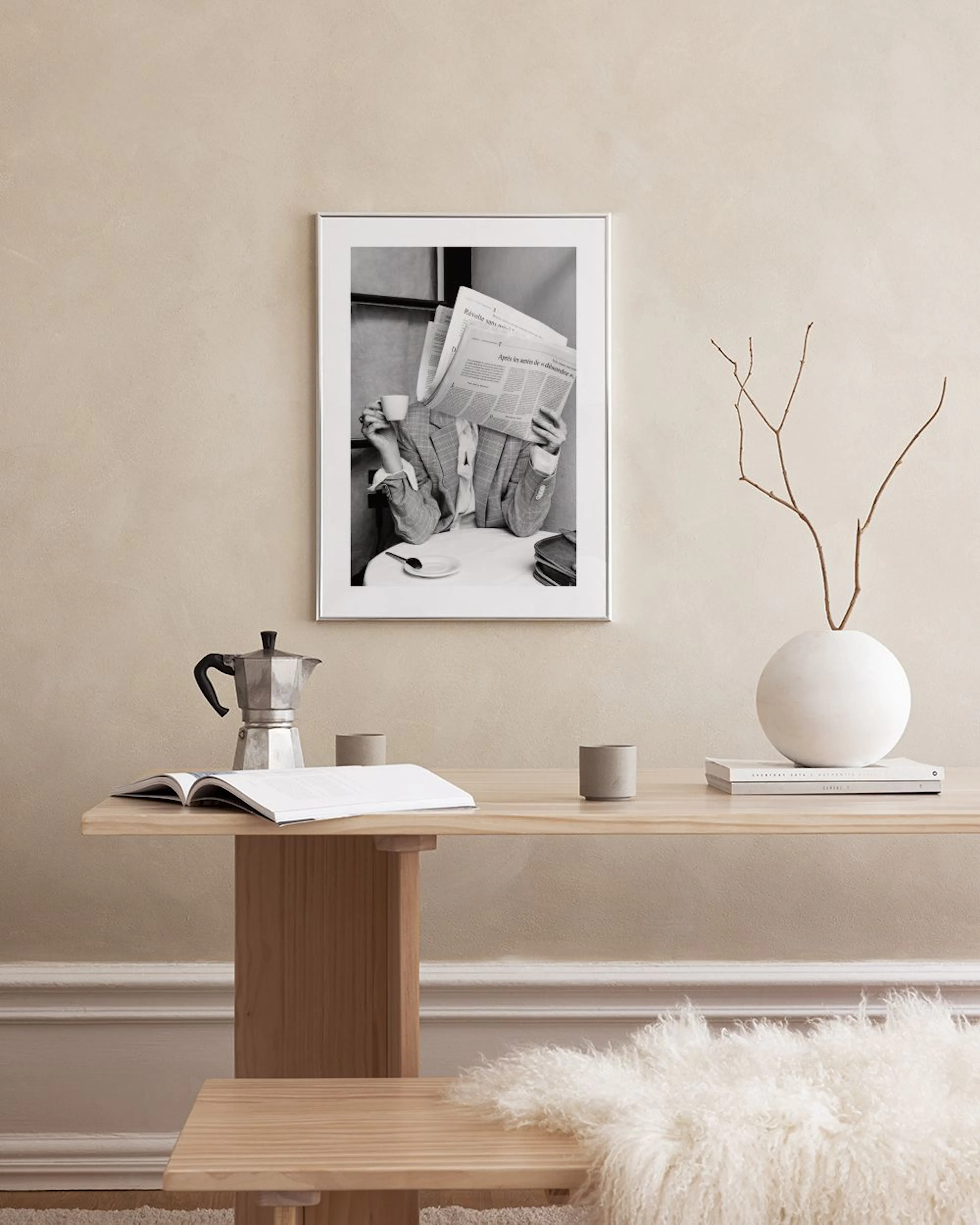 Plakat med svart-hvitt fotografi av person som leser avis med kaffekopp, plassert på en grå benk.