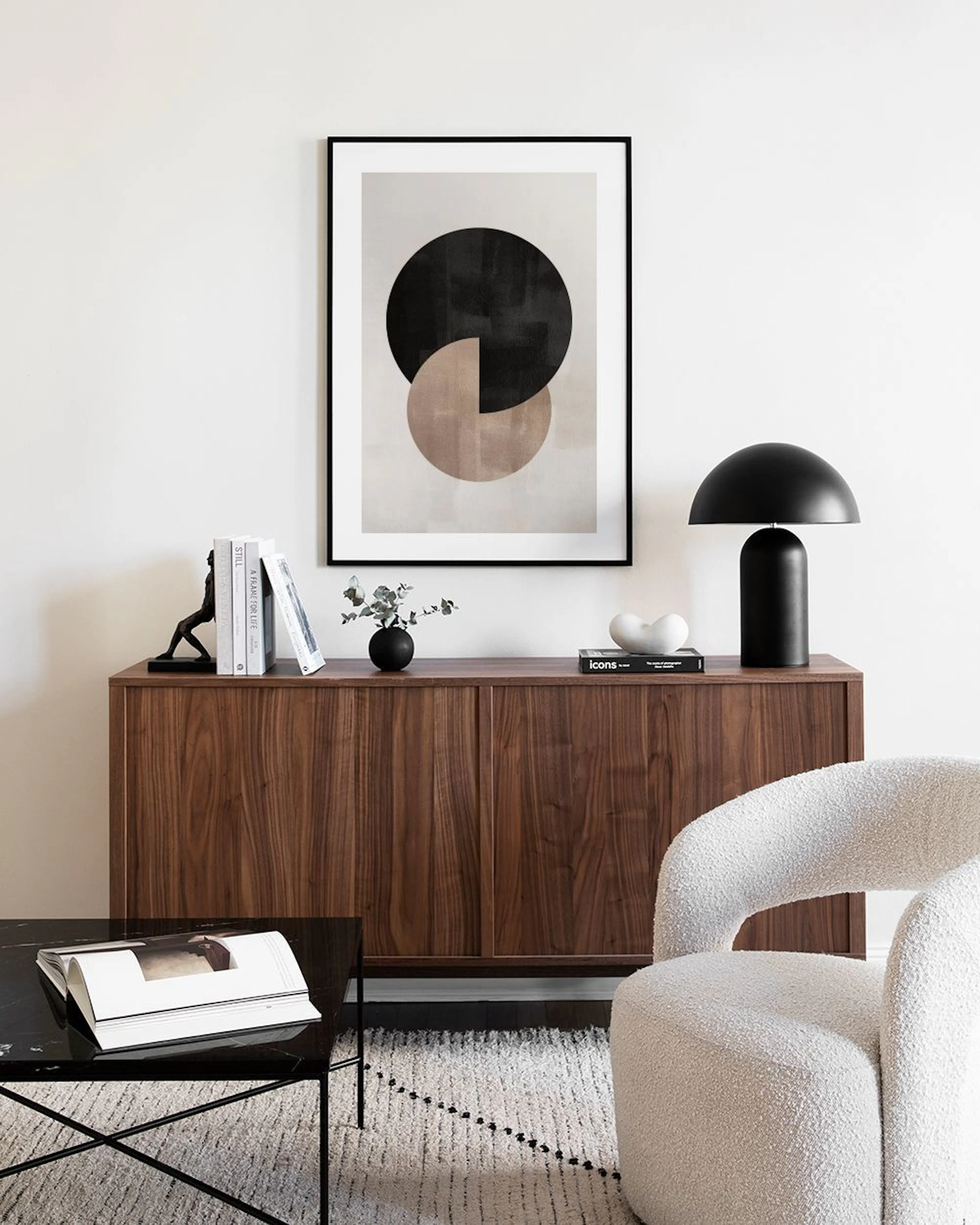 Plakat med to overlappende sirkler i svart og beige, henger på en grå vegg ved en hvit kommode og en stol.