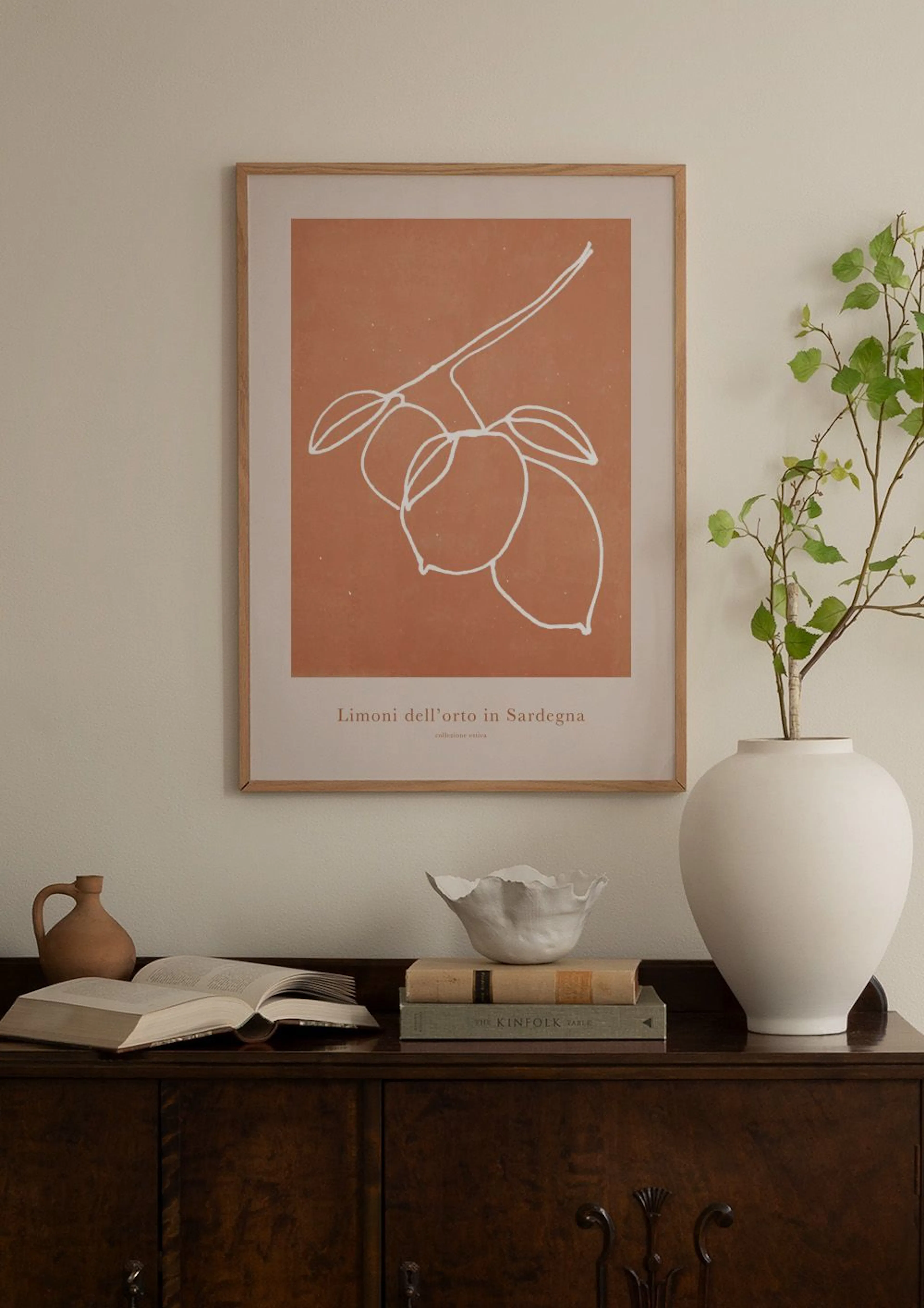 A print of white line art lemons on a terracotta background, hanging above a white cabinet with decorative vases.