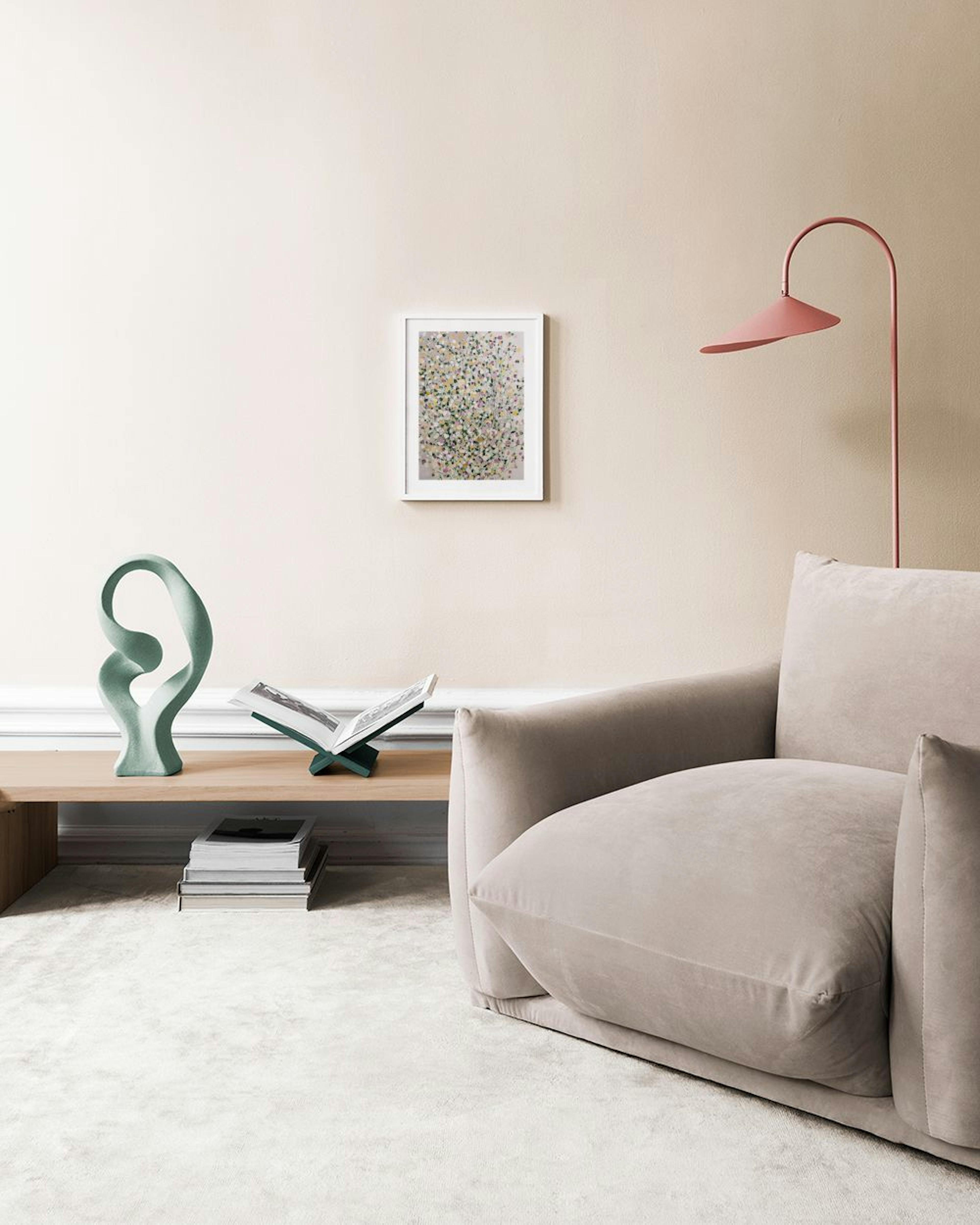 A print of a flower bush with colorful leaves in yellow, green, and pink, hanging above a white marble side table.
