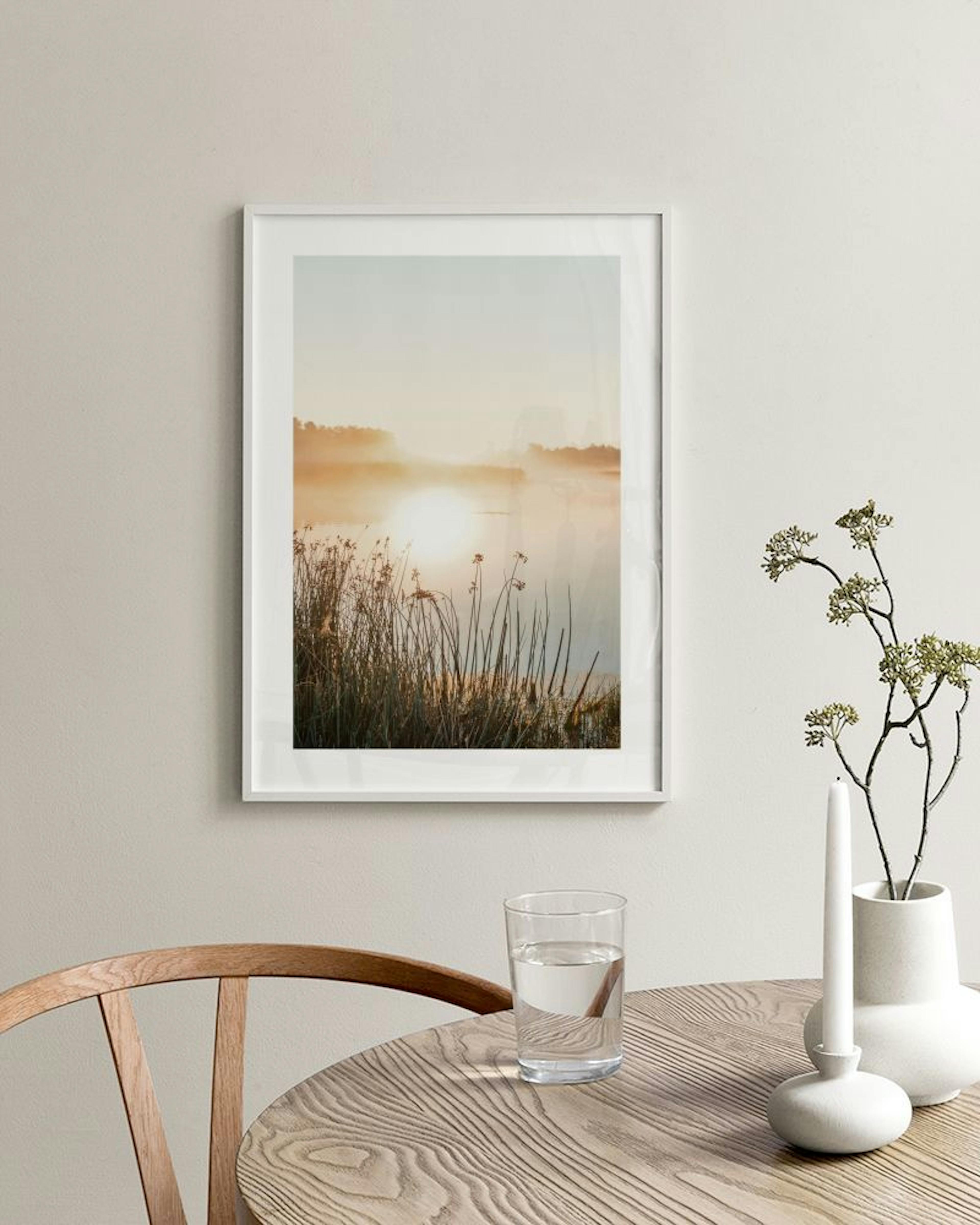 Affiche lac brumeux au lever du soleil avec roseaux, suspendue au-dessus dun meuble bas blanc avec vases et livres.