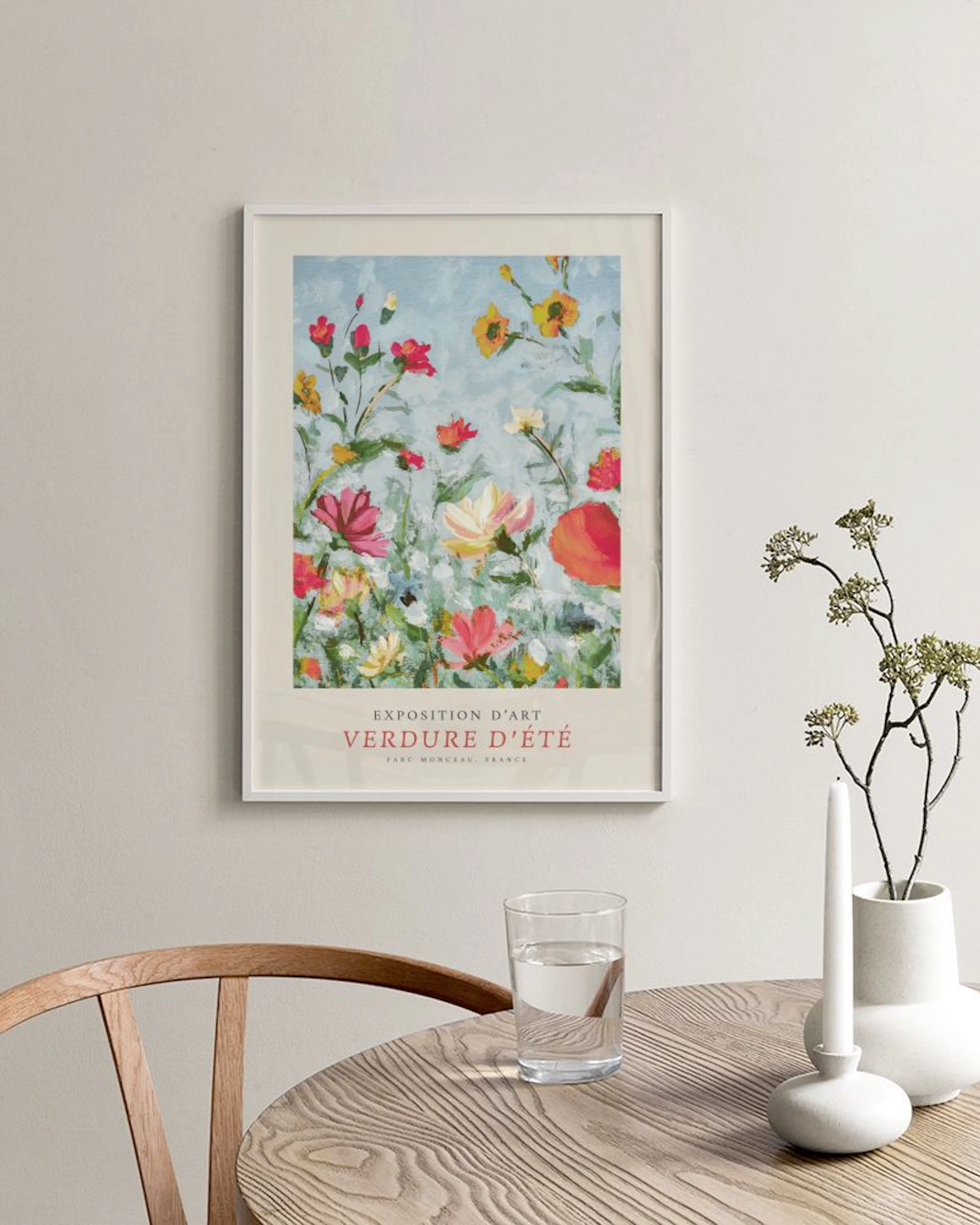 A colorful floral print with red, yellow, and pink flowers on a light blue background, hanging above a white marble table.