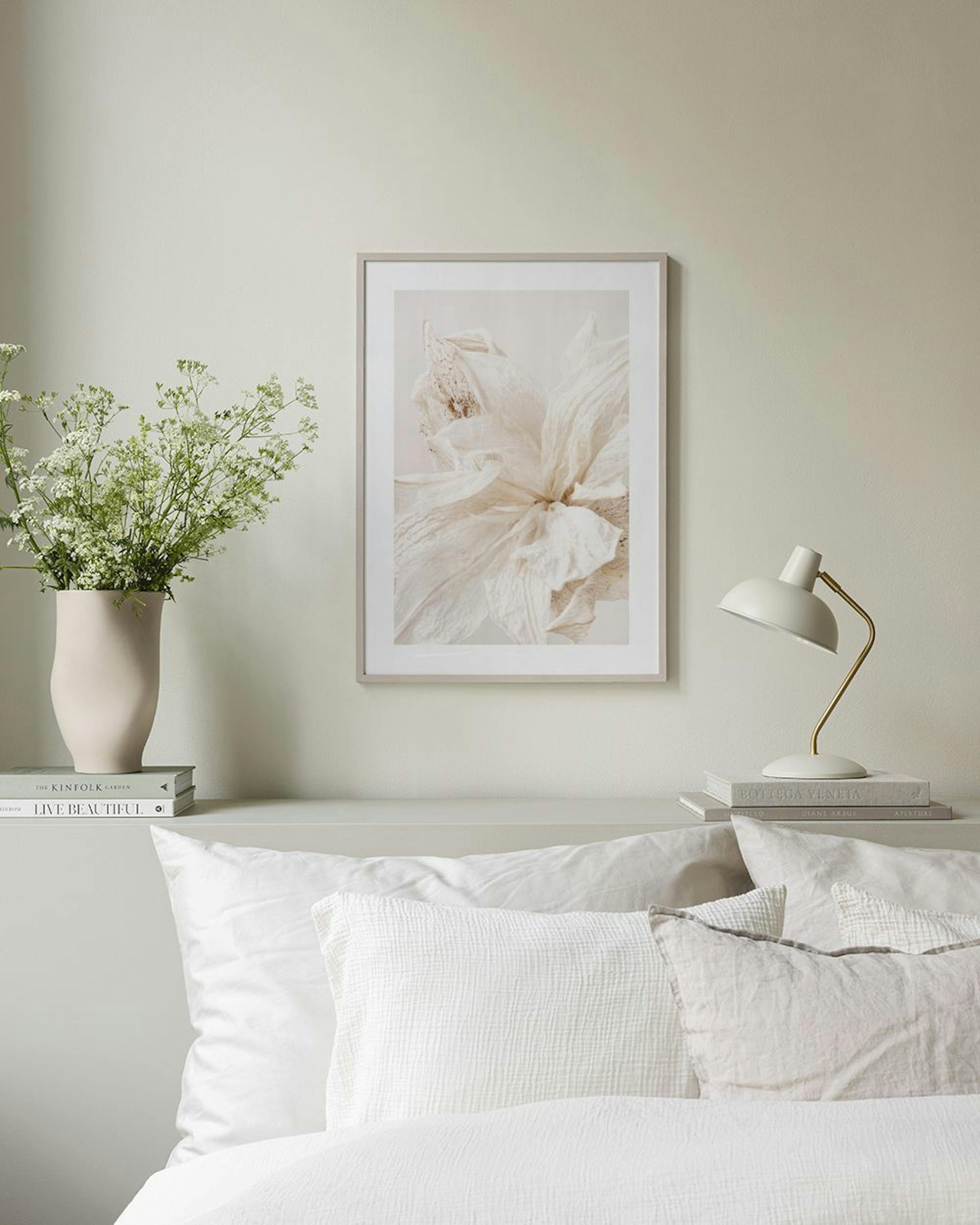 A print of a dried beige flower with delicate petals, hanging above a white cabinet with decorative vases and books.