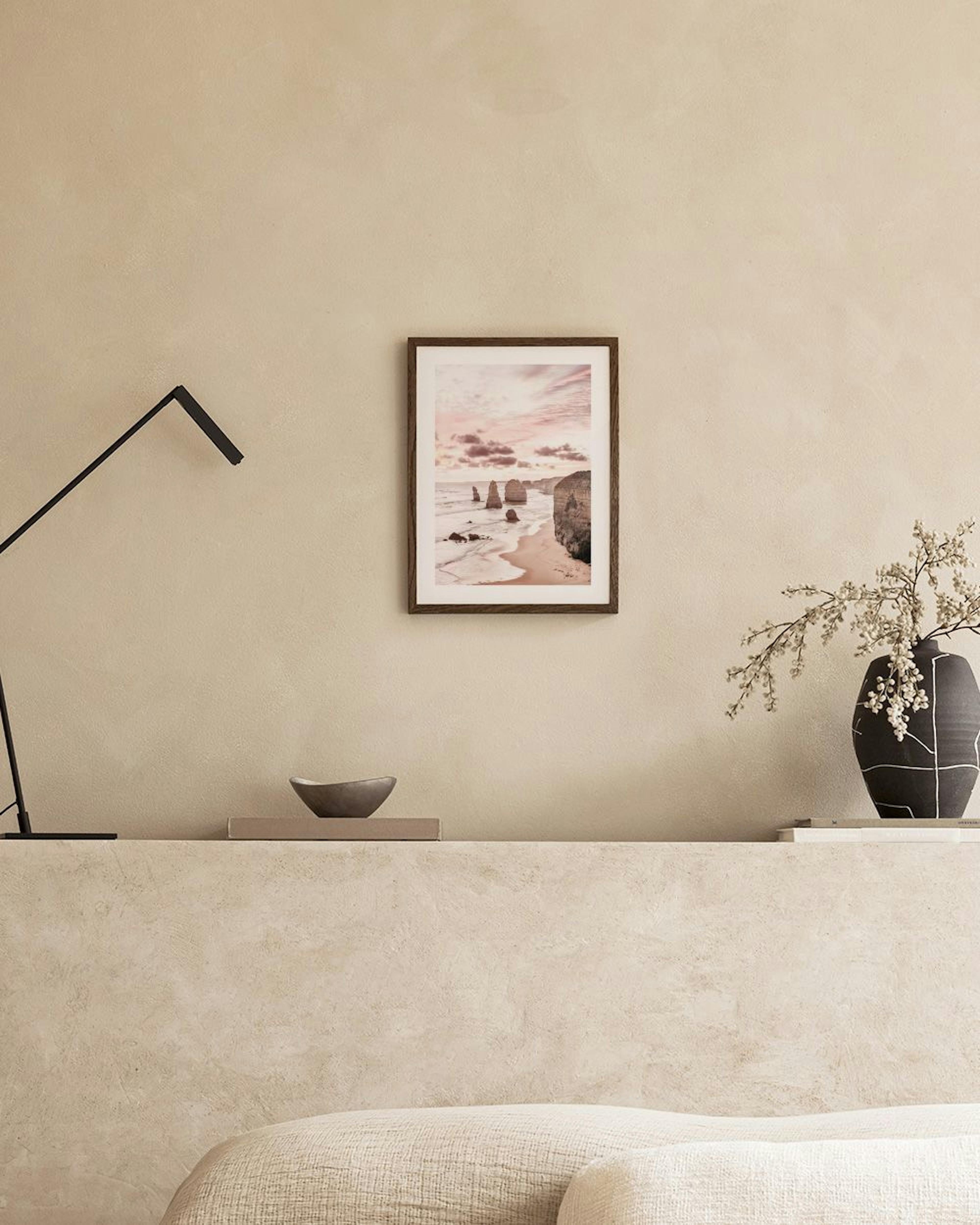 Affiche de falaises océaniques au coucher du soleil, exposée sur un meuble blanc avec un vase et un livre ouvert.