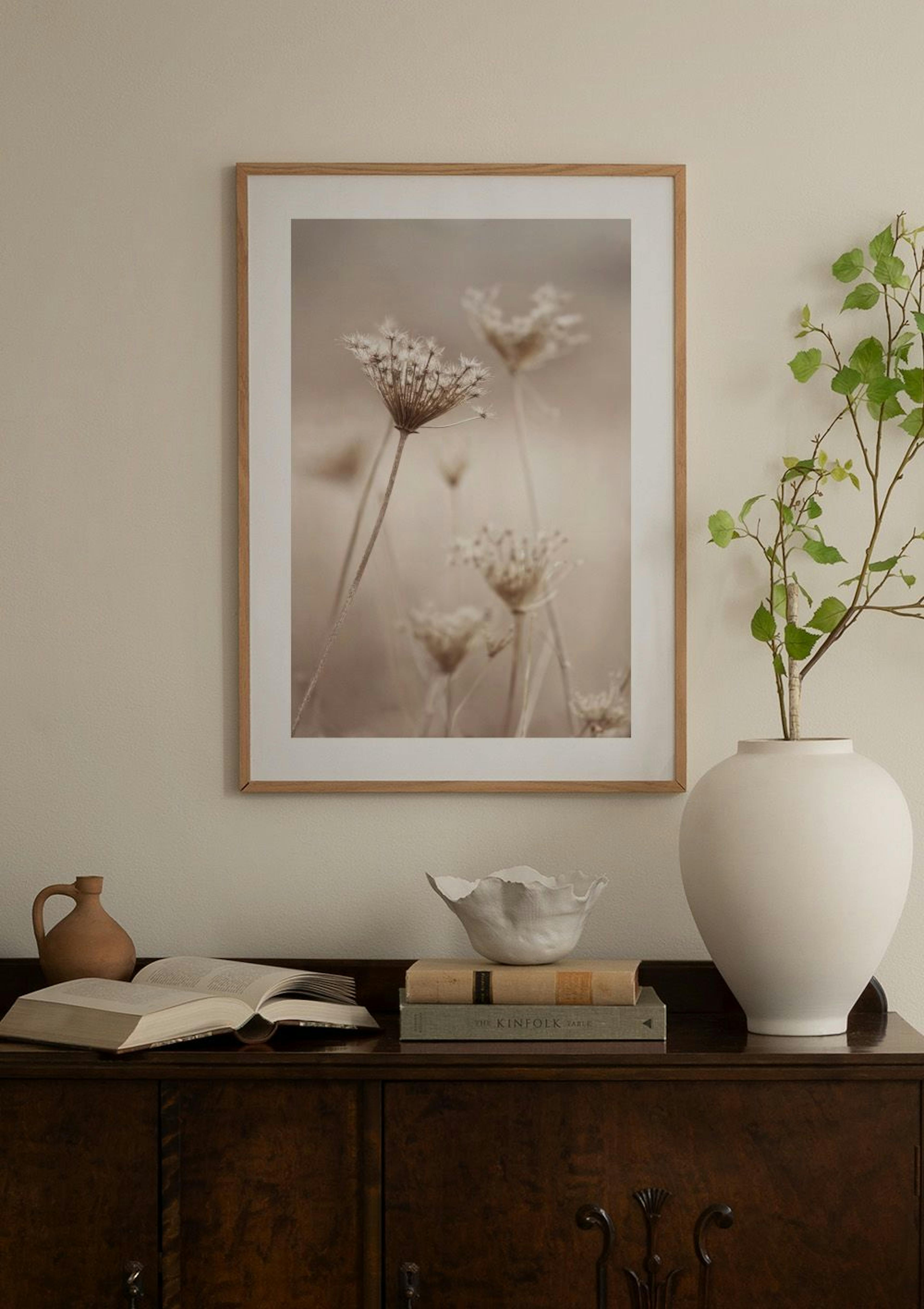 淡いベージュの壁に飾られた、茶色の枯れた植物が写るポスター。ラタン製のキャビネットの上に置かれた書籍や花瓶と共に、温かみのある空間を演出しています。