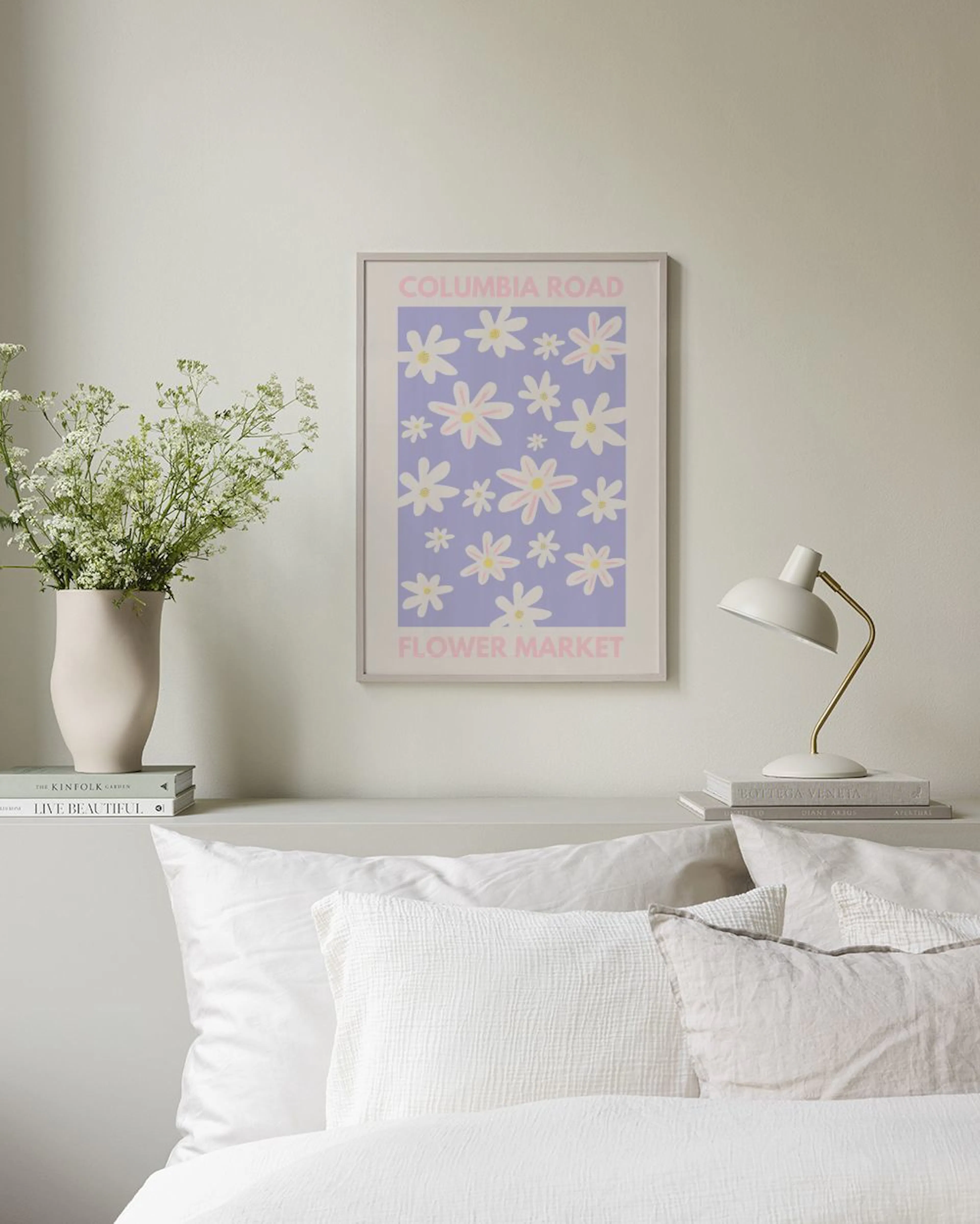 Poster Flower Market mit weißen Blumen auf Lila, hängt über einem weißen Beistelltisch mit Schale und einem rosa Hocker.