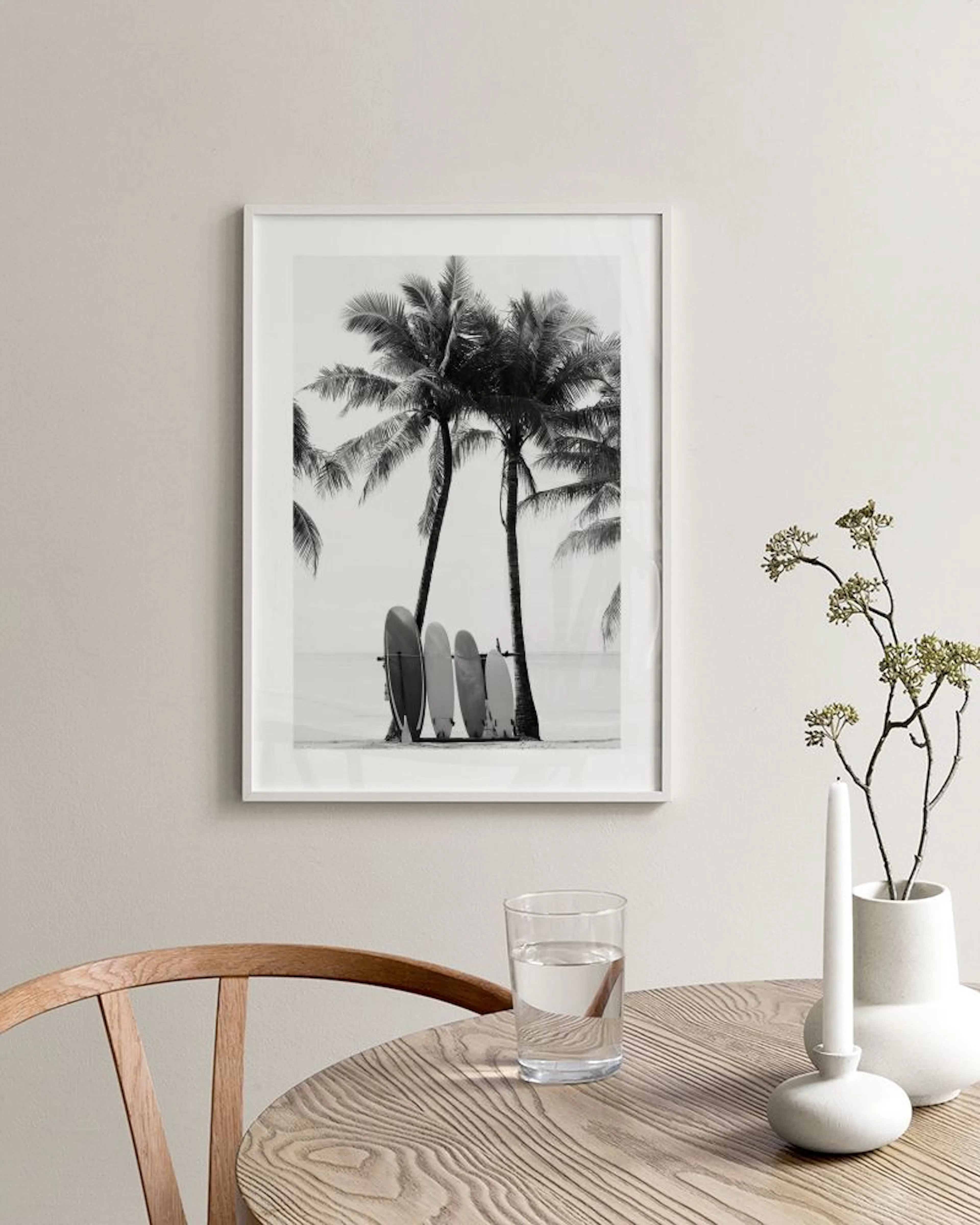 Black and white print of surfboards leaning against palm trees on a beach, hanging in a modern living room.
