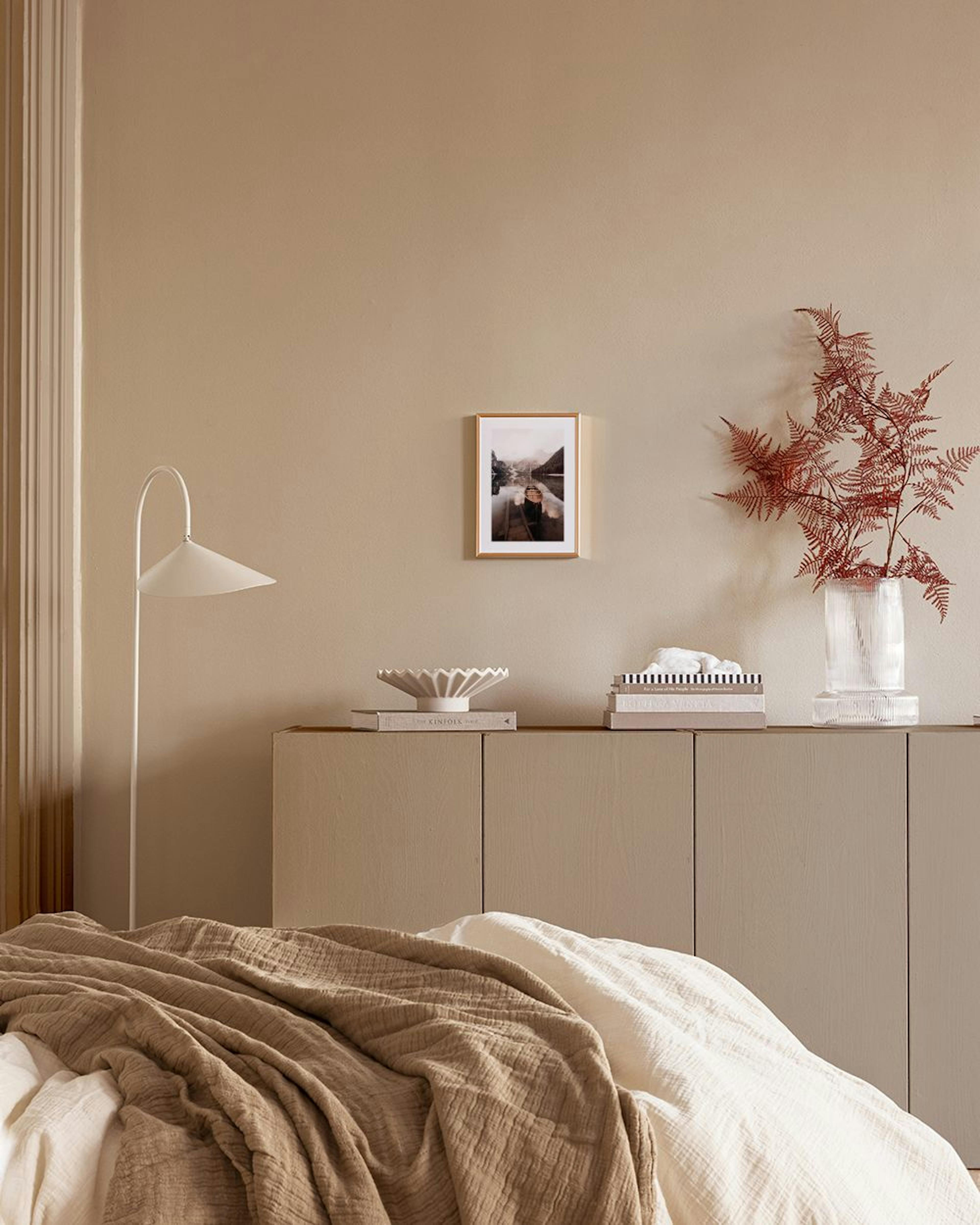 A stunning print of a boat on a calm lake with mountains in the background, displayed in a modern living room with a beige armch