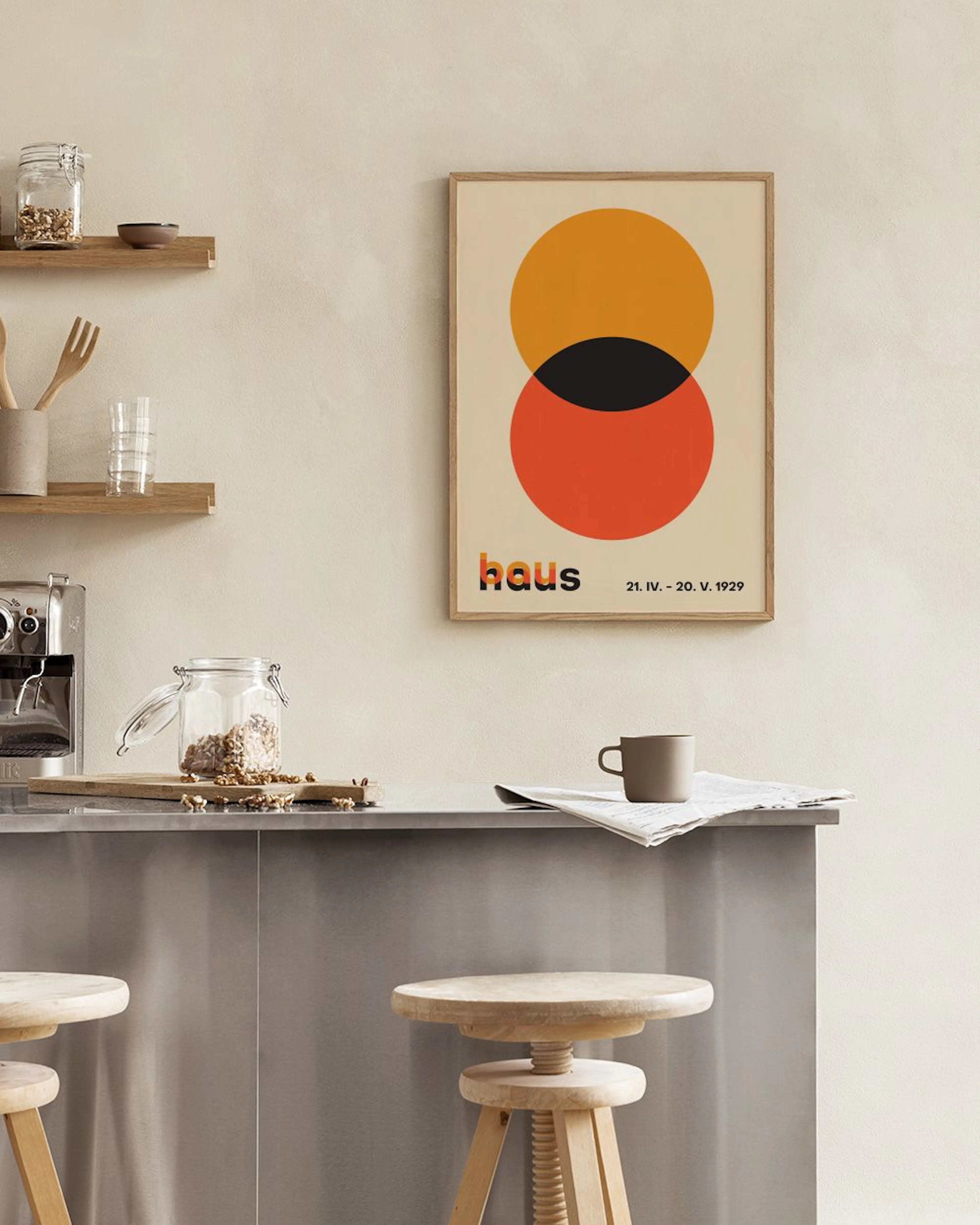 En Bauhaus-inspirerad poster med orange och röda cirklar som överlappar en svart form, hängandes ovanför ett svart hyllplan med 