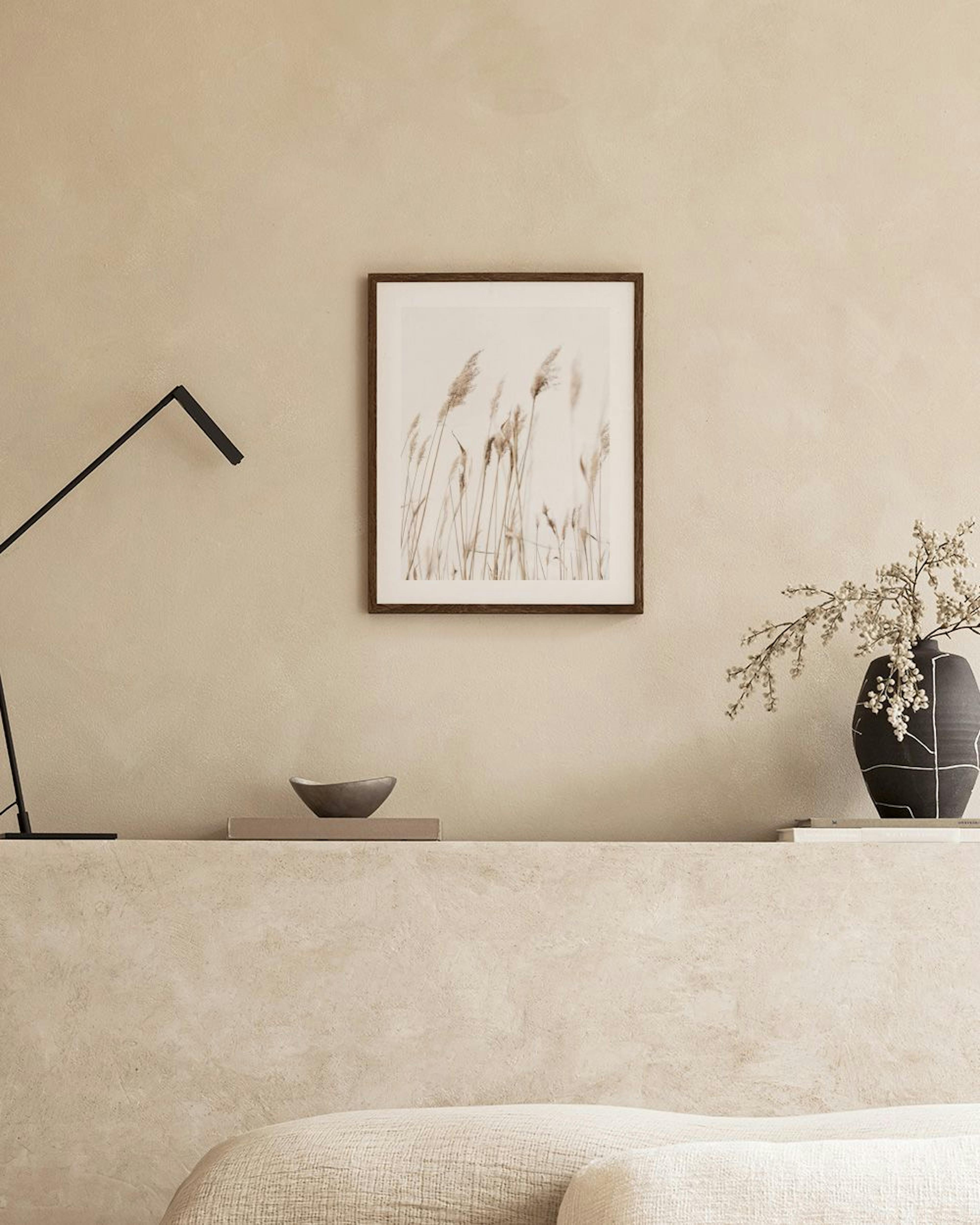 Póster de cañas secas sobre fondo blanco, colgado sobre un sillón beige en una habitación moderna.