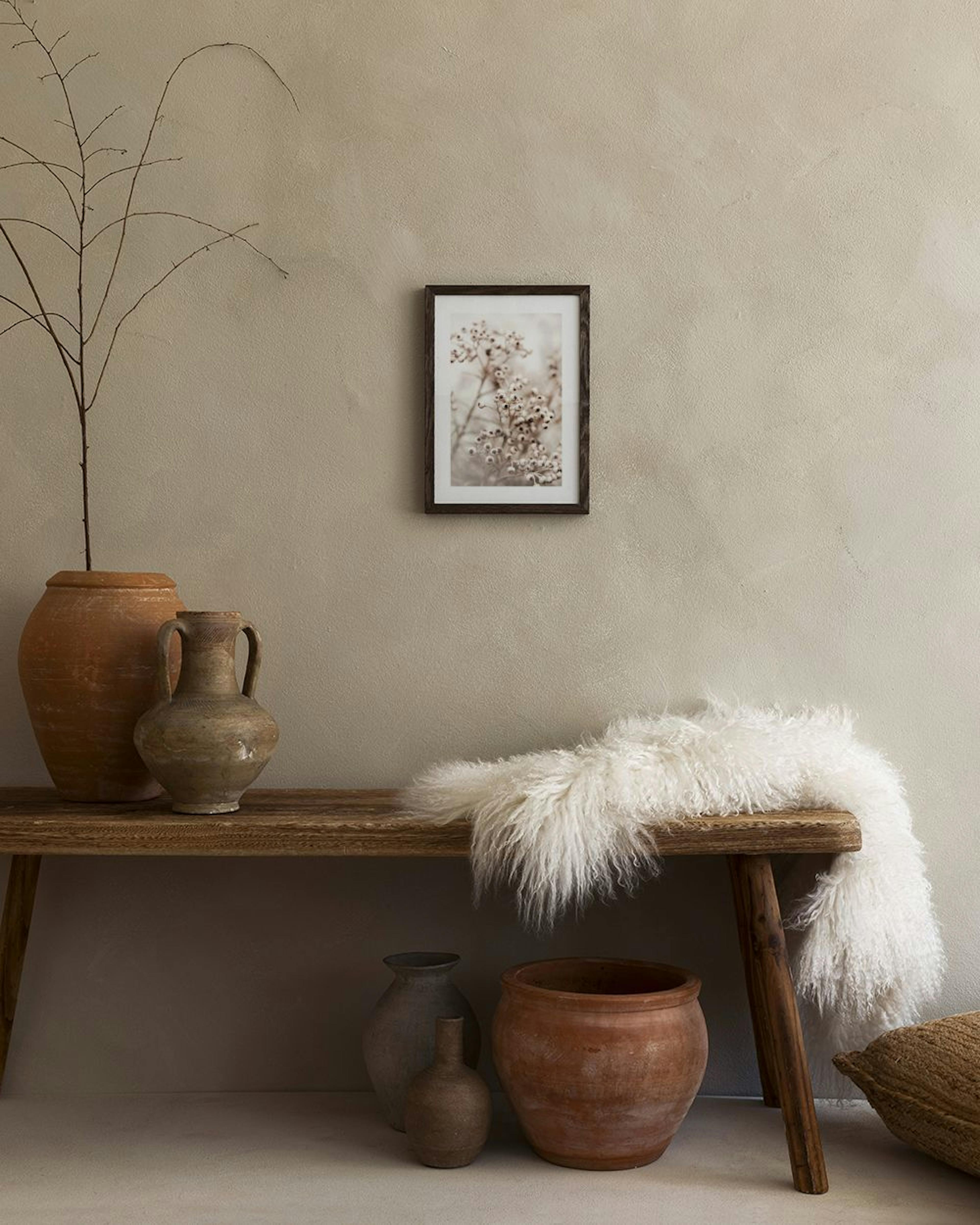 Poster van beige bessen aan takken, hangend boven een wit bijzettafeltje met twee vazen en boeken.