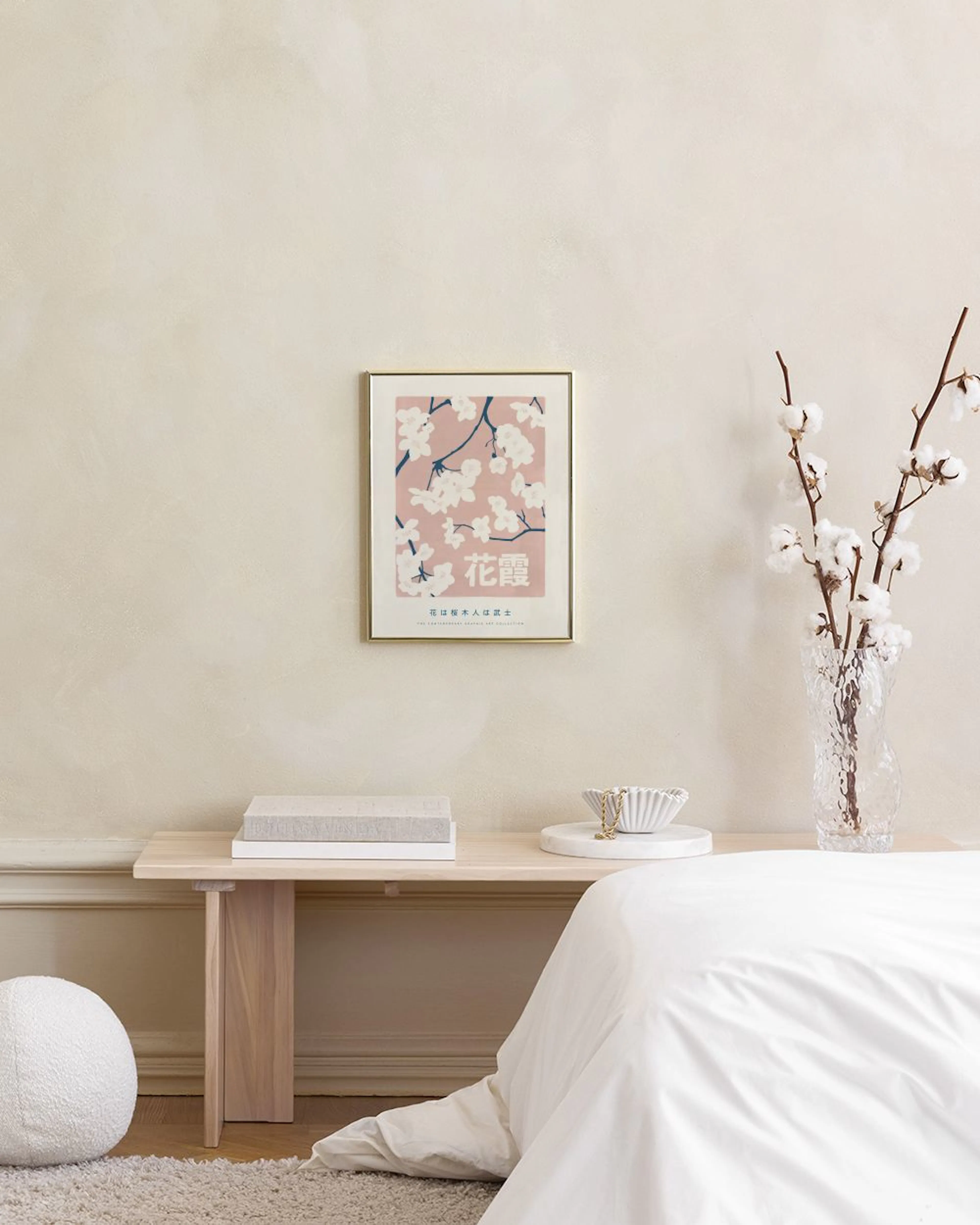 Poster mit japanischen Kirschblüten auf rosafarbenem Grund, hängend über einem Beistelltisch mit Vasen und Büchern.