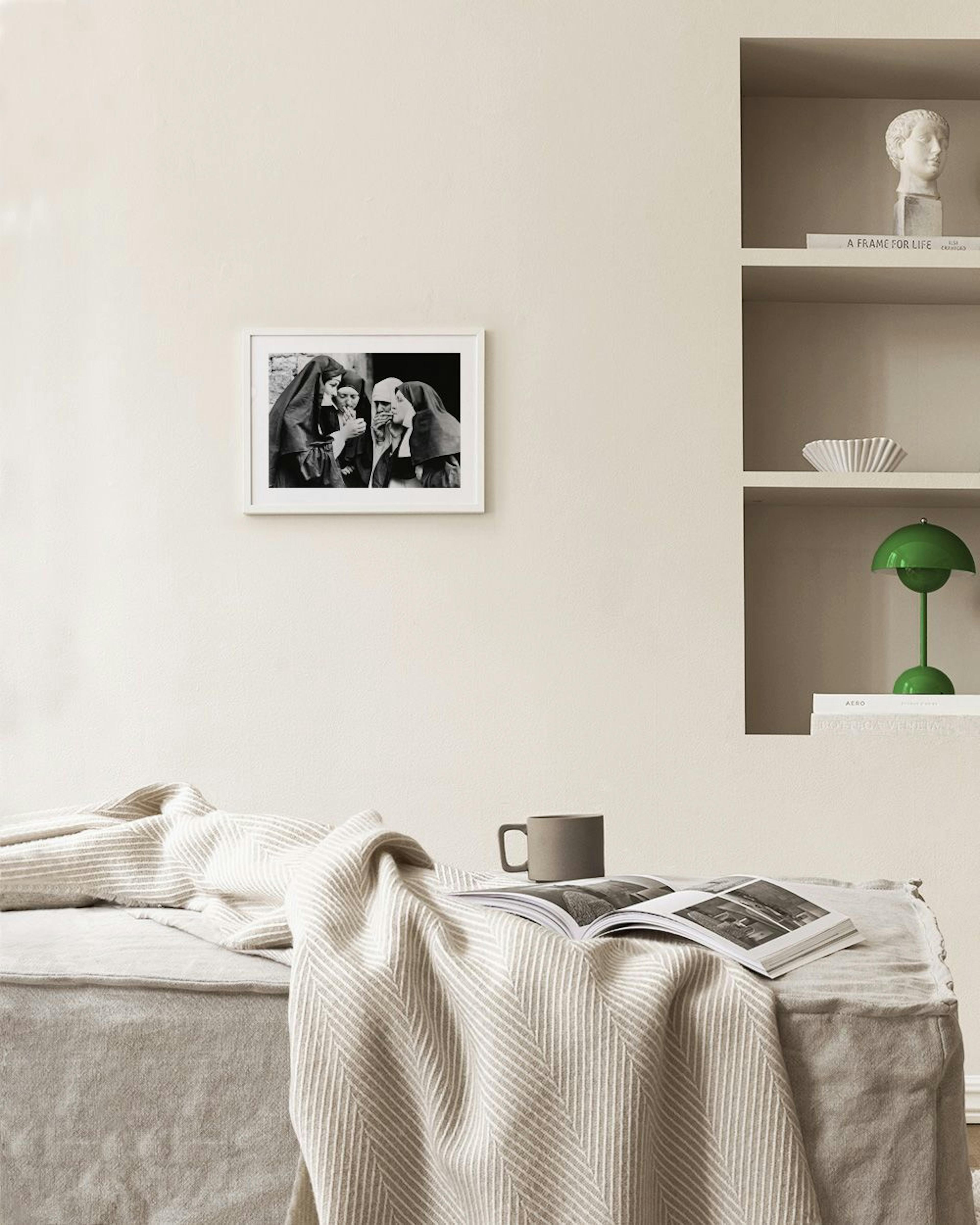 Black and white print of four nuns in habits, one lighting a cigarette for another, hanging above a side table with decorative s