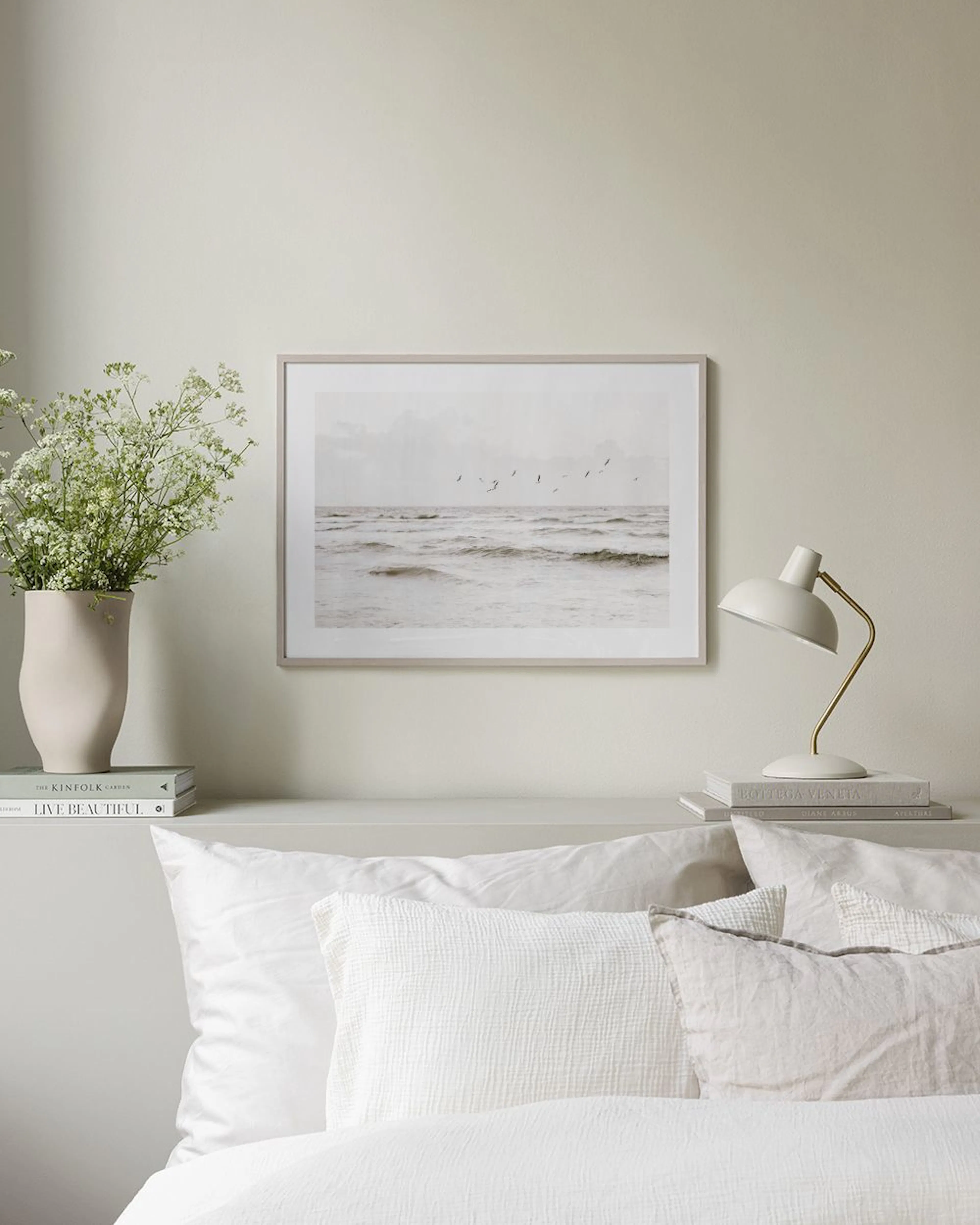 A print of a monochrome stormy sea with birds flying above, displayed in a minimal living room above a side table.