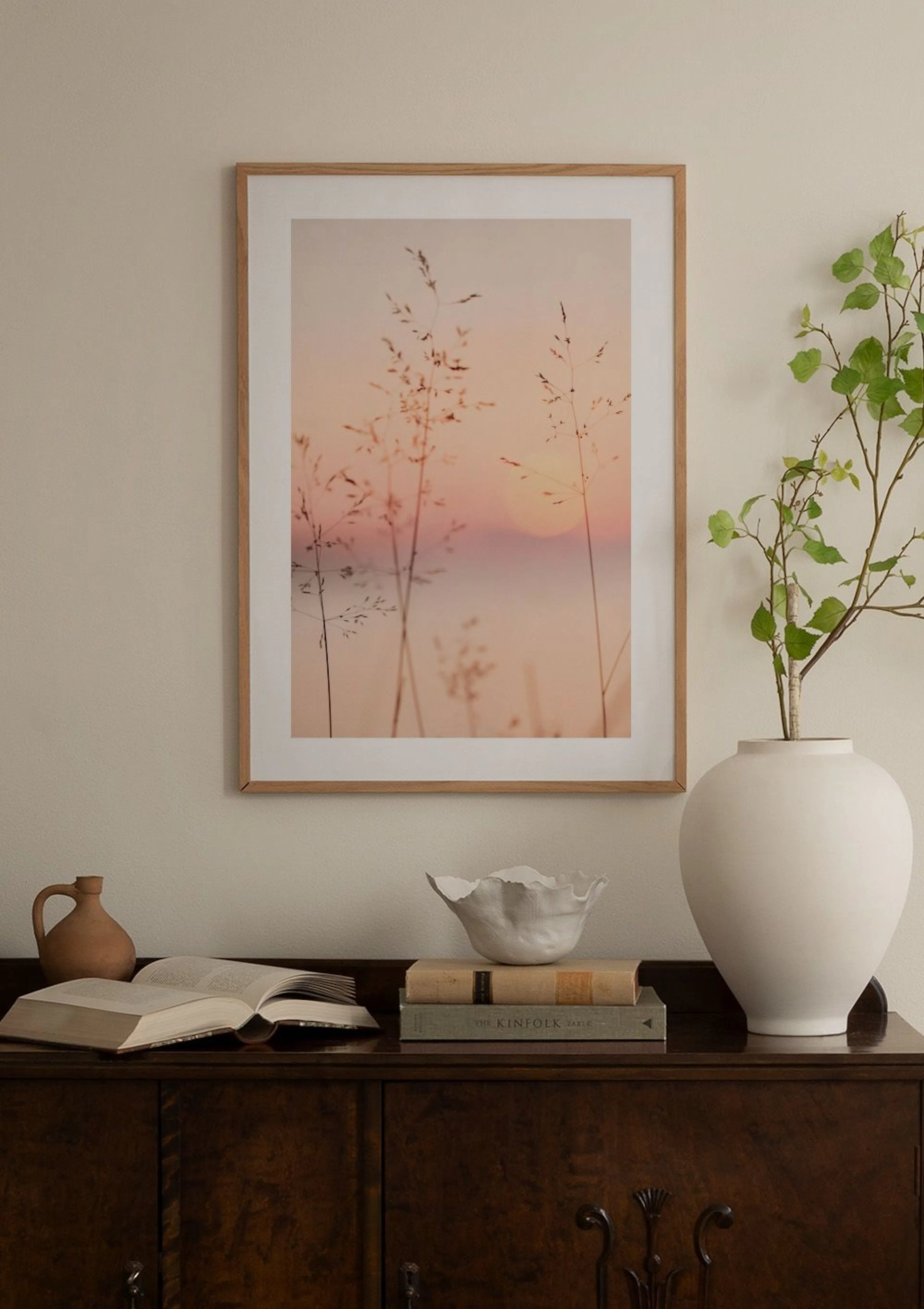 Plakat med solnedgang og strå, henger over en lilla fløyelsstol i et rom med en hvit pidestall og vase.
