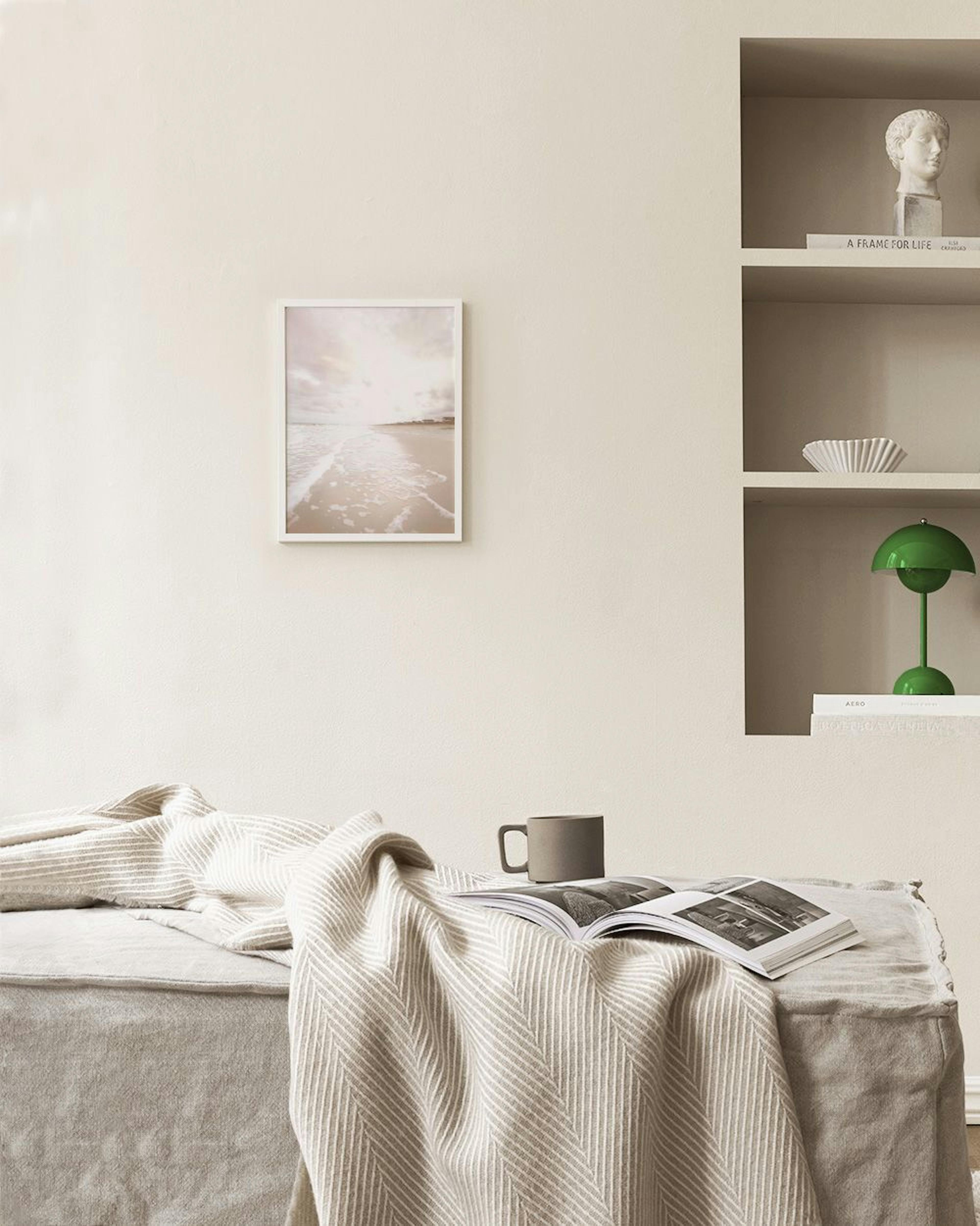 Poster mit hellem Strand und Meereswellen unter bewölktem Himmel, über einem Sideboard mit Vasen und Büchern.
