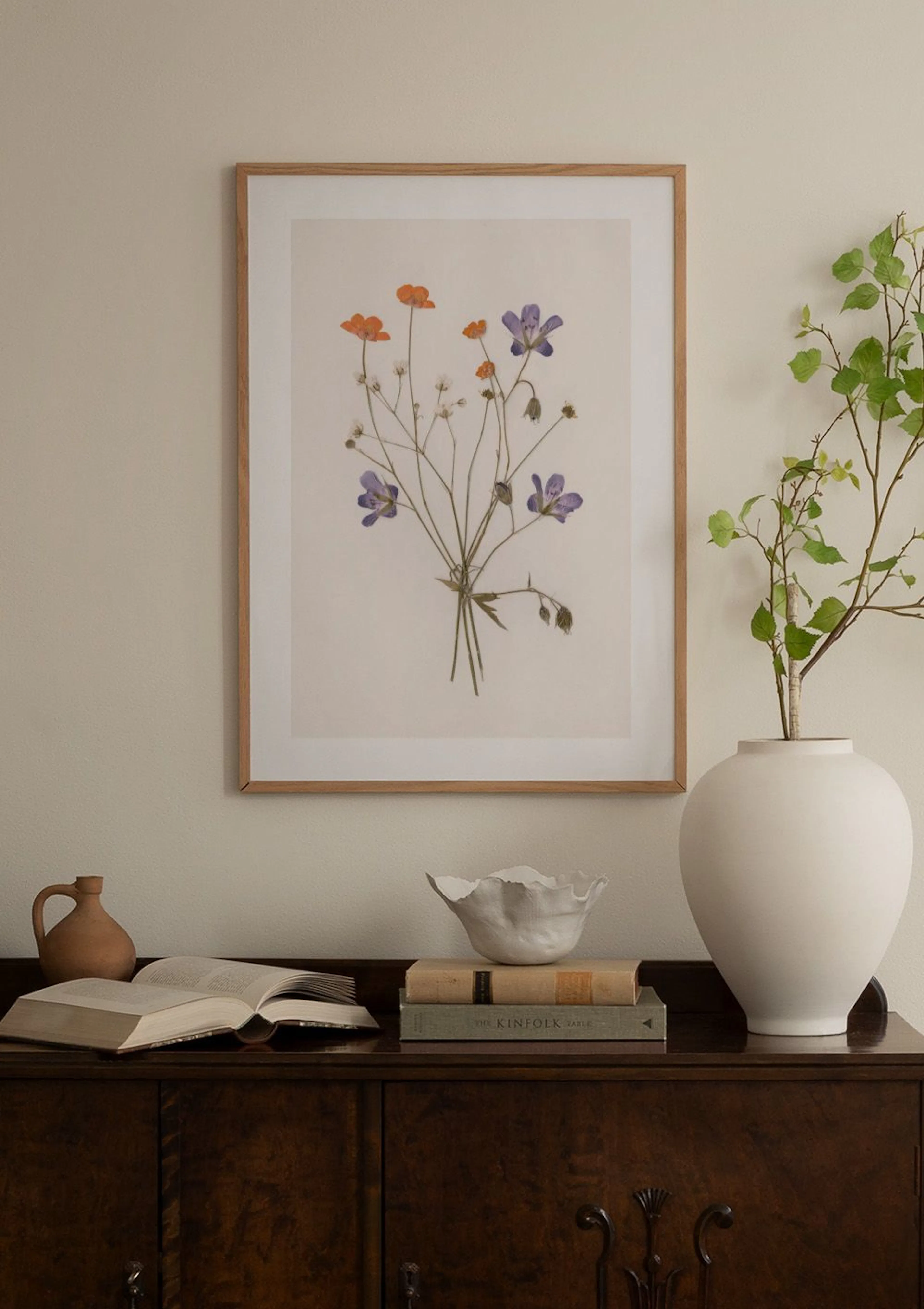 A botanical print of dried orange and purple wildflowers displayed on a white wall above a marble side table.