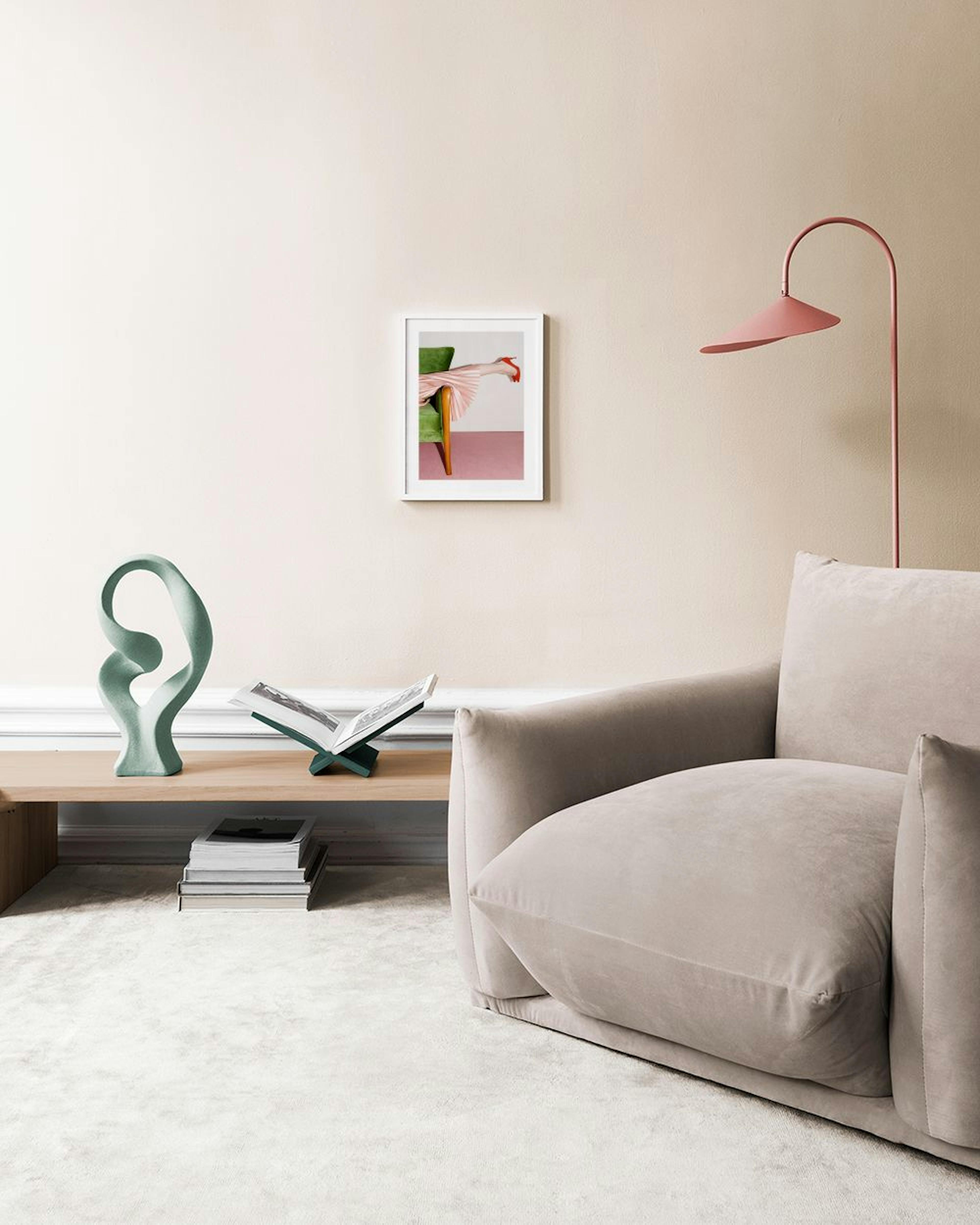 Poster van een been in een roze plissérok en rode hakken, liggend op een groene stoel, hangend boven een wit dressoir.